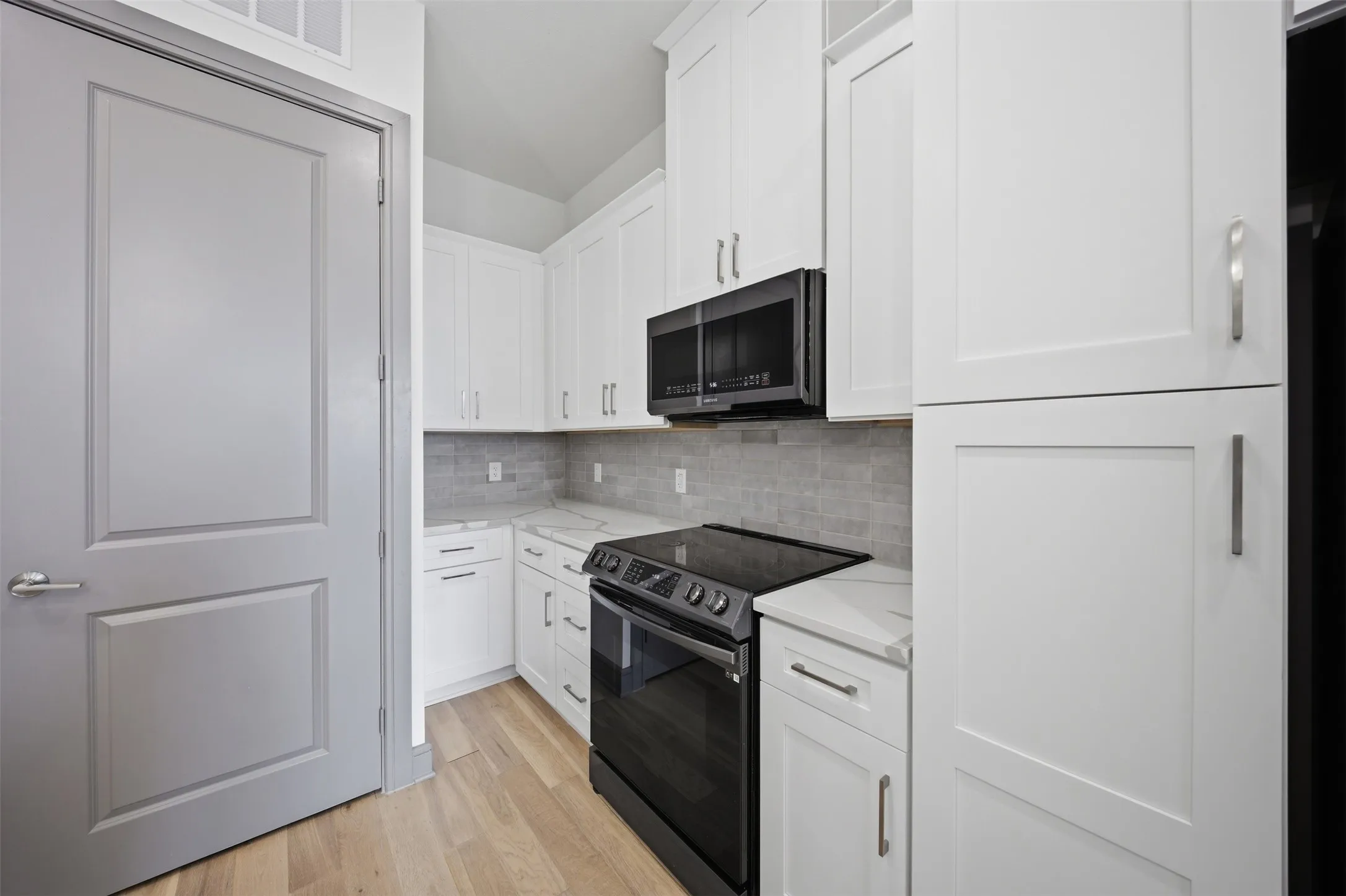 Kitchen featuring white shaker-style cabinetry, a tile backsplash, light wood-finish flooring, and a black range and microwave