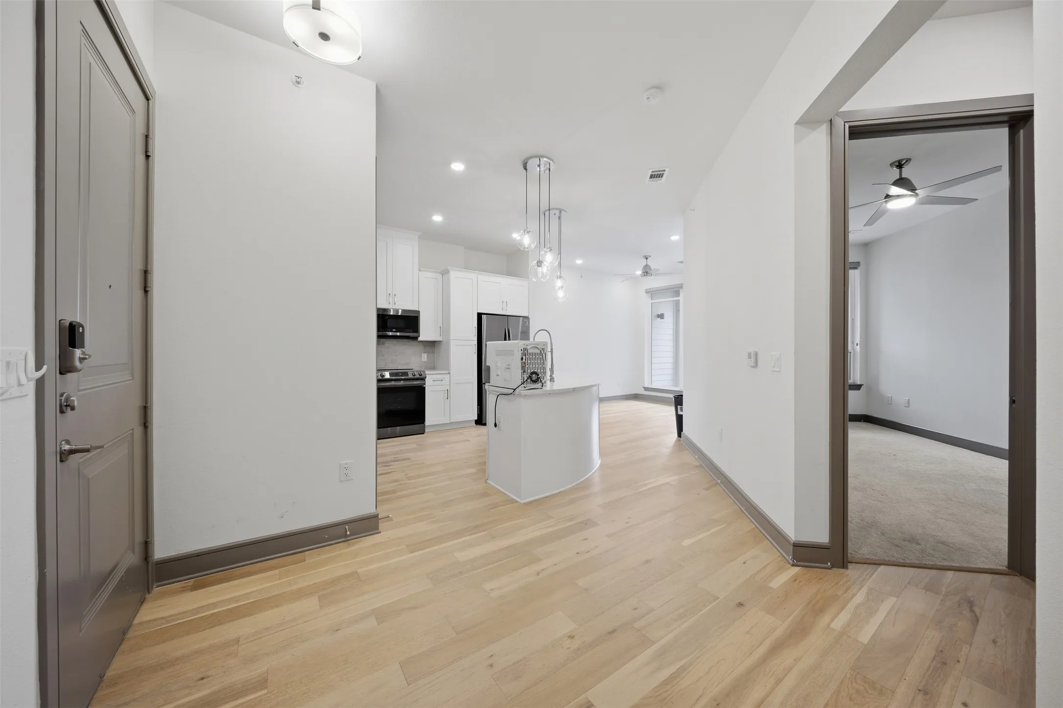 Wood-finish flooring, white cabinetry, integrated stainless steel appliances, and a curved kitchen island with pendant lighting