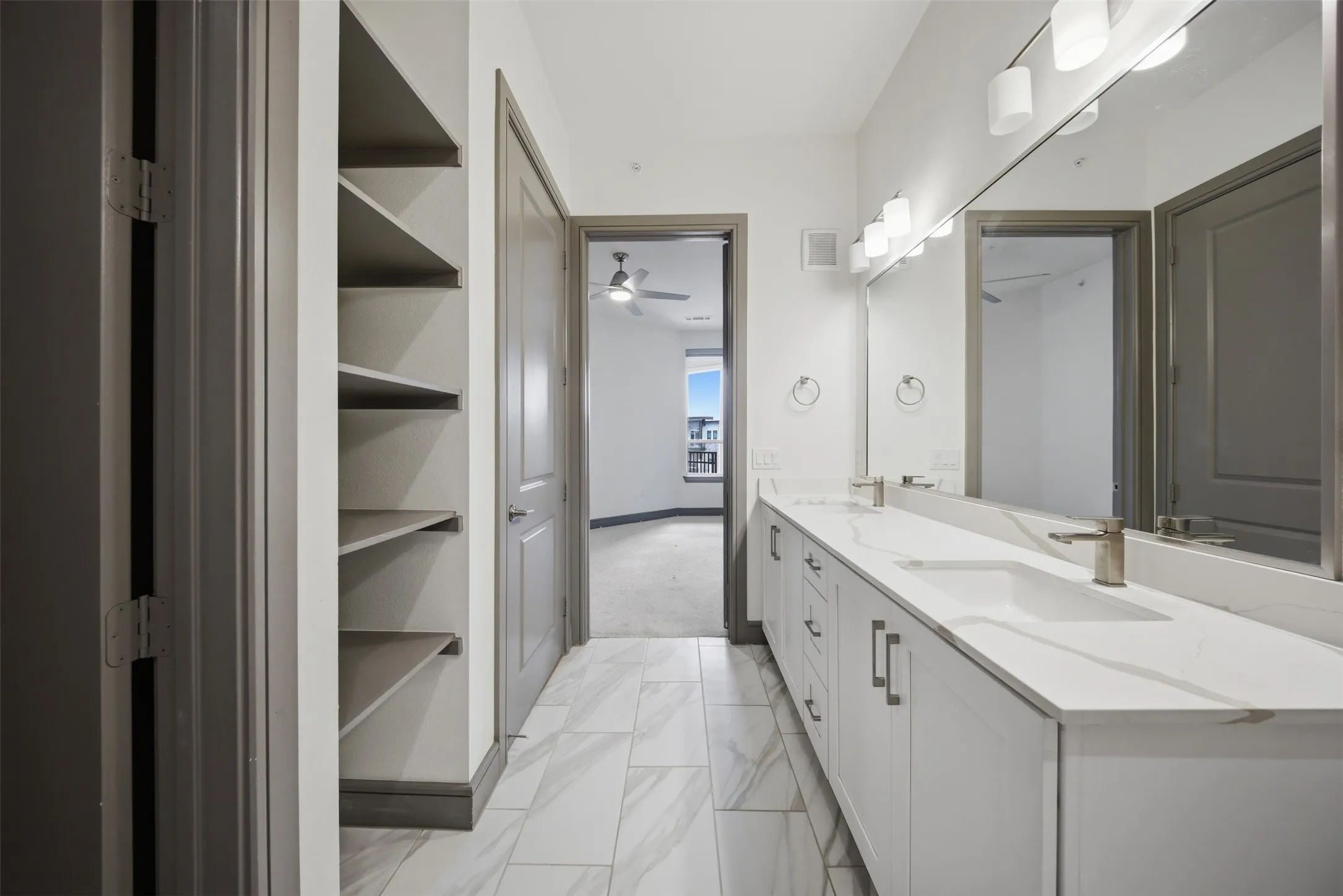 Dual vanity with integrated sinks and brushed nickel faucets, extensive counter space, large wall-mounted mirror, white shaker-style cabinetry, and built-in shelving