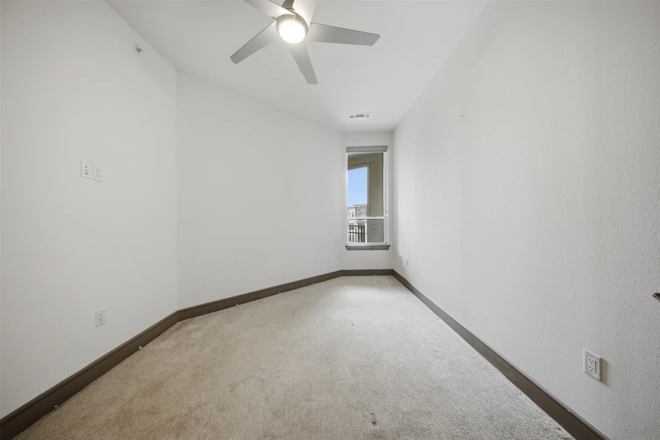 Recessed window with exterior balcony access, ceiling fan, and light-toned carpeting