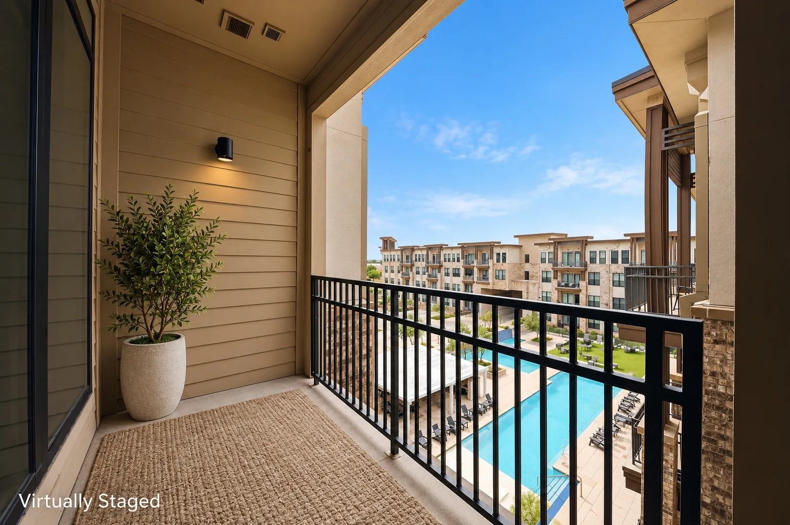 Balcony with horizontal siding, exterior sconce lighting, and black metal railing overlooking a swimming pool and multi-story buildings