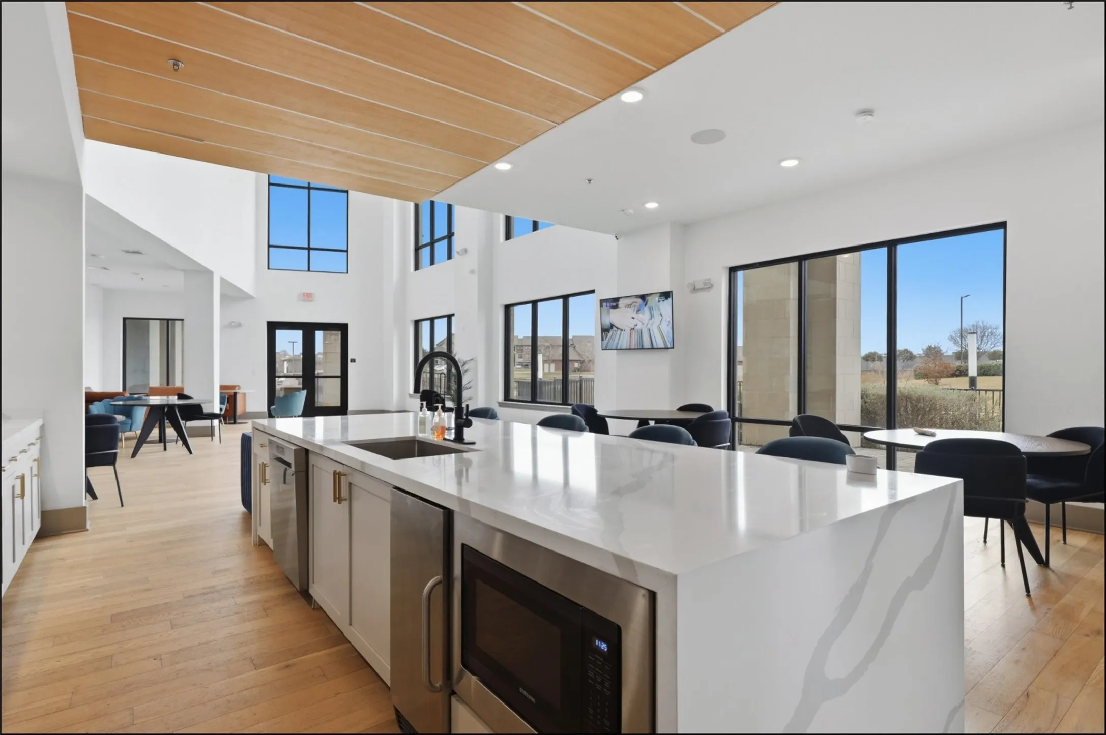 Spacious common area featuring a large kitchen island with integrated sink, stainless steel appliances, wood-finish flooring, and expansive windows