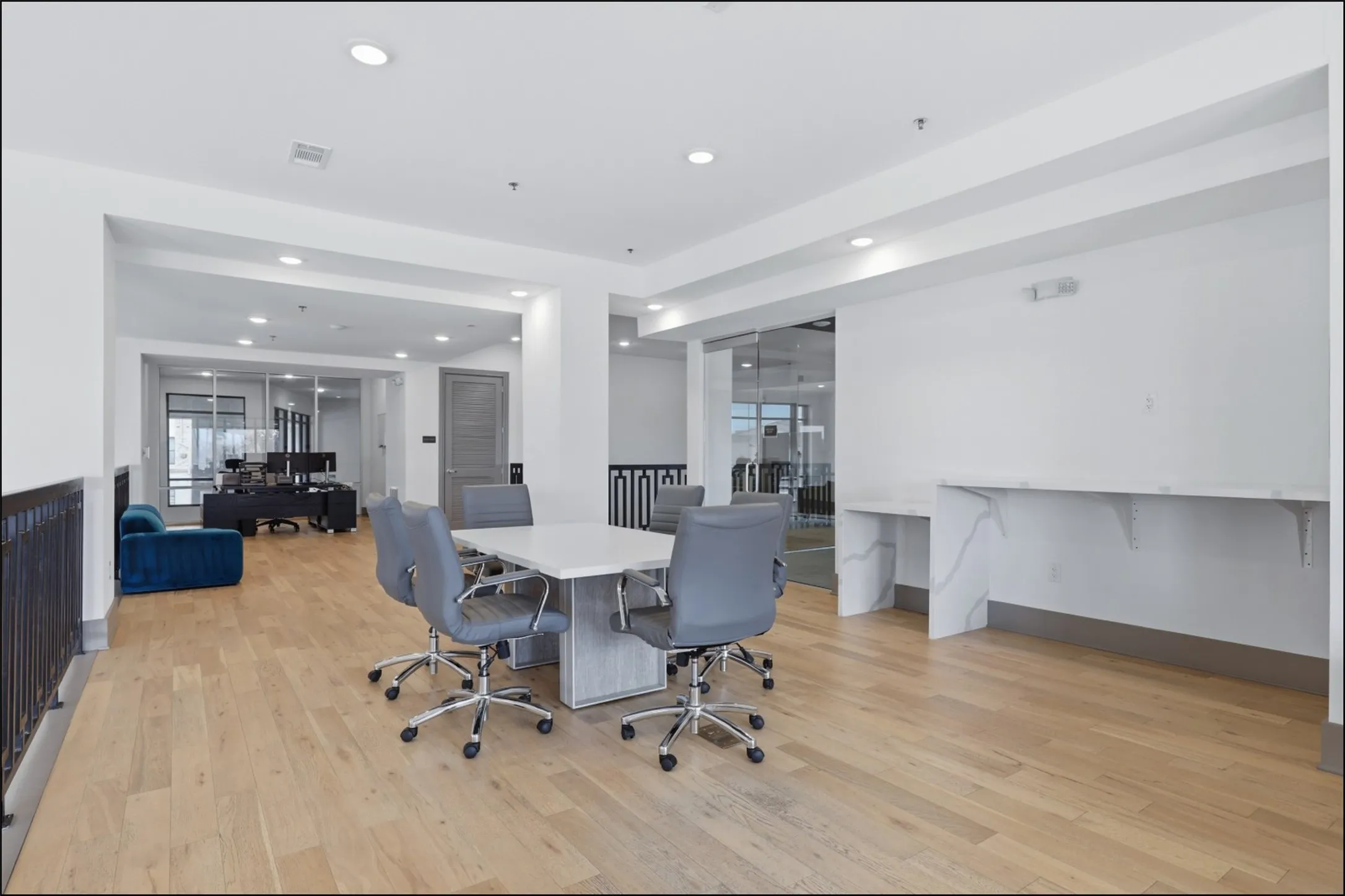 Spacious open-concept area featuring light wood-finish flooring, recessed lighting, and a white wall-mounted desk with a stone-finish countertop