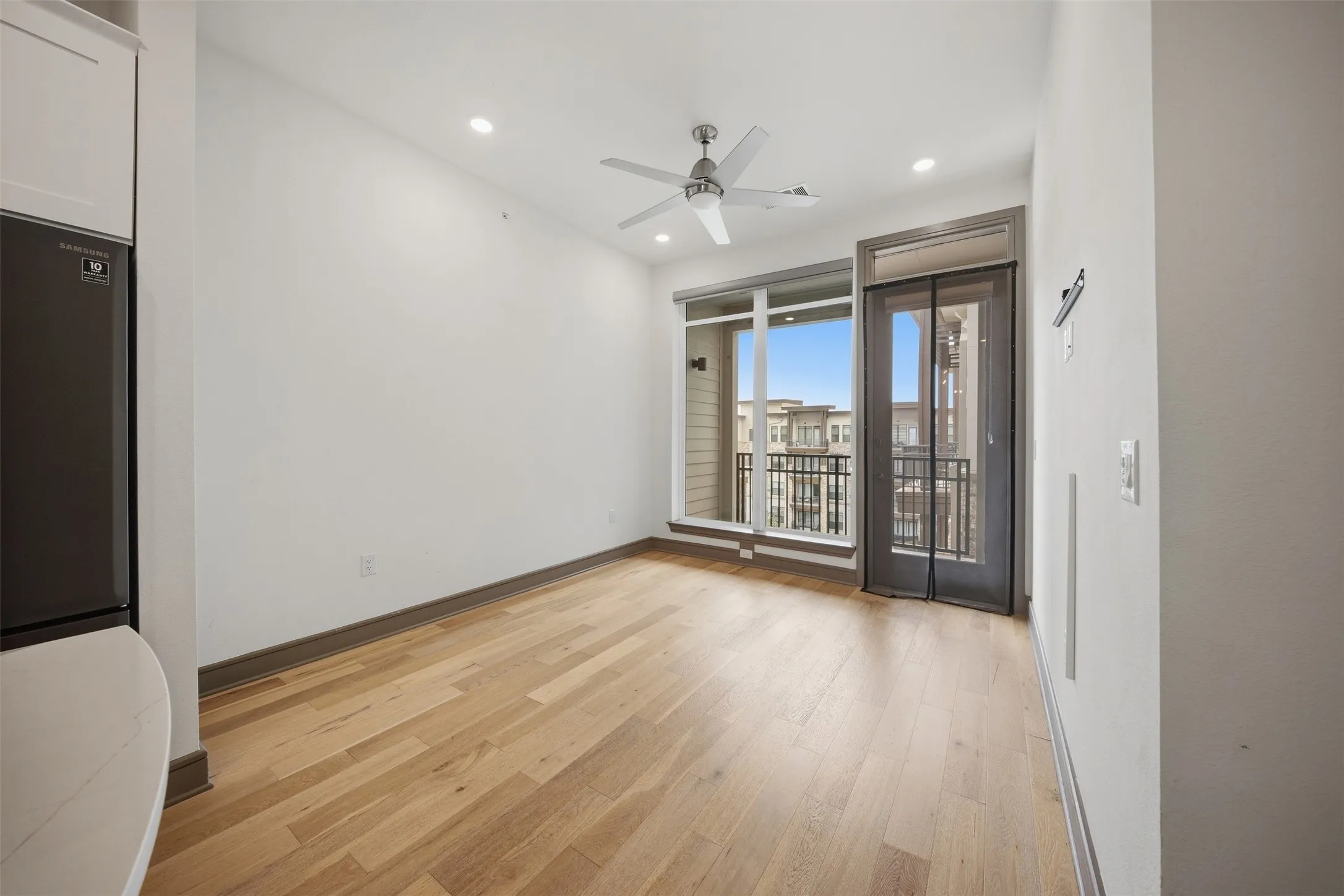 Light wood-finish flooring, recessed lighting, ceiling fan, full-height window, and glass-panel door to a balcony