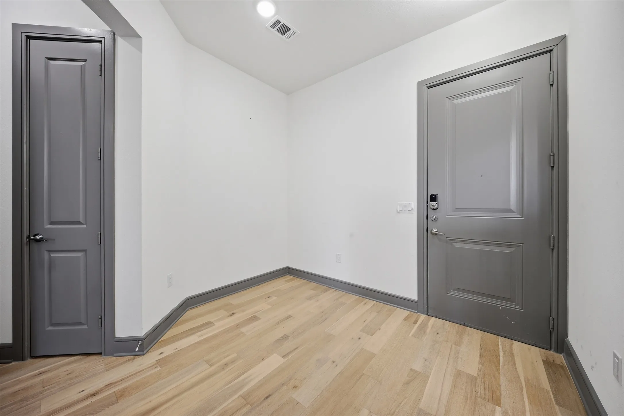 Wood-finish flooring, white walls, recessed ceiling light, paneled doors, and grey trim throughout