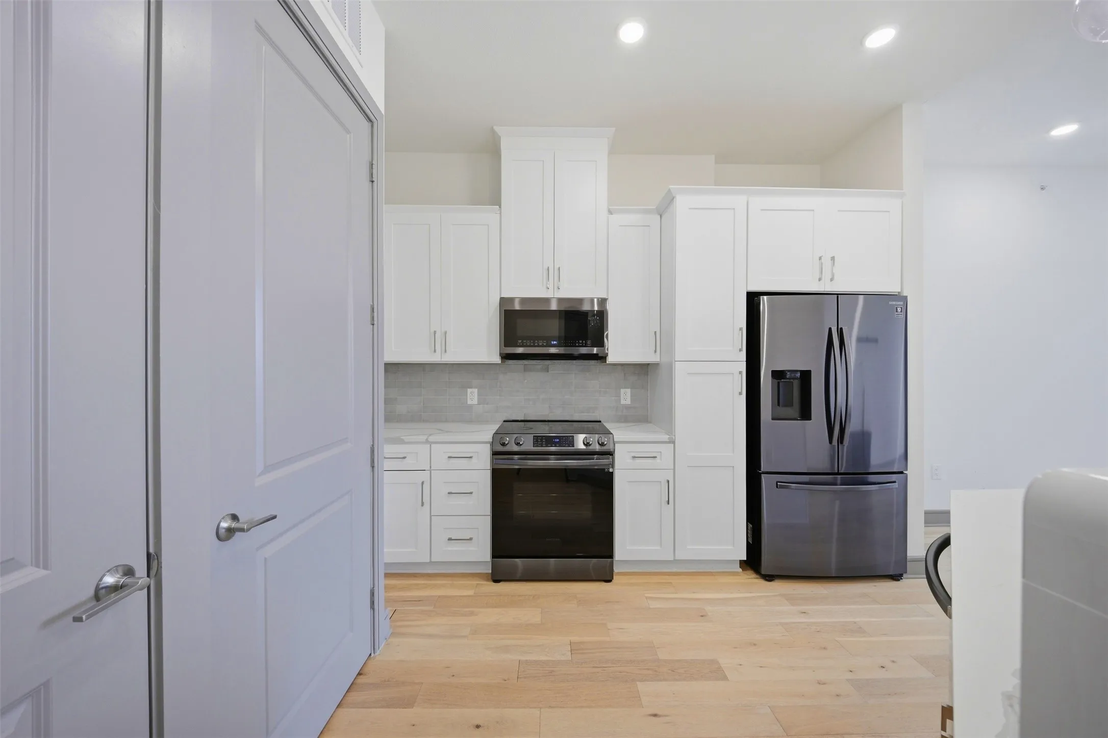 Modern kitchen featuring white shaker cabinetry, stainless steel appliances, light wood-finish flooring, recessed lighting, and a tile backsplash