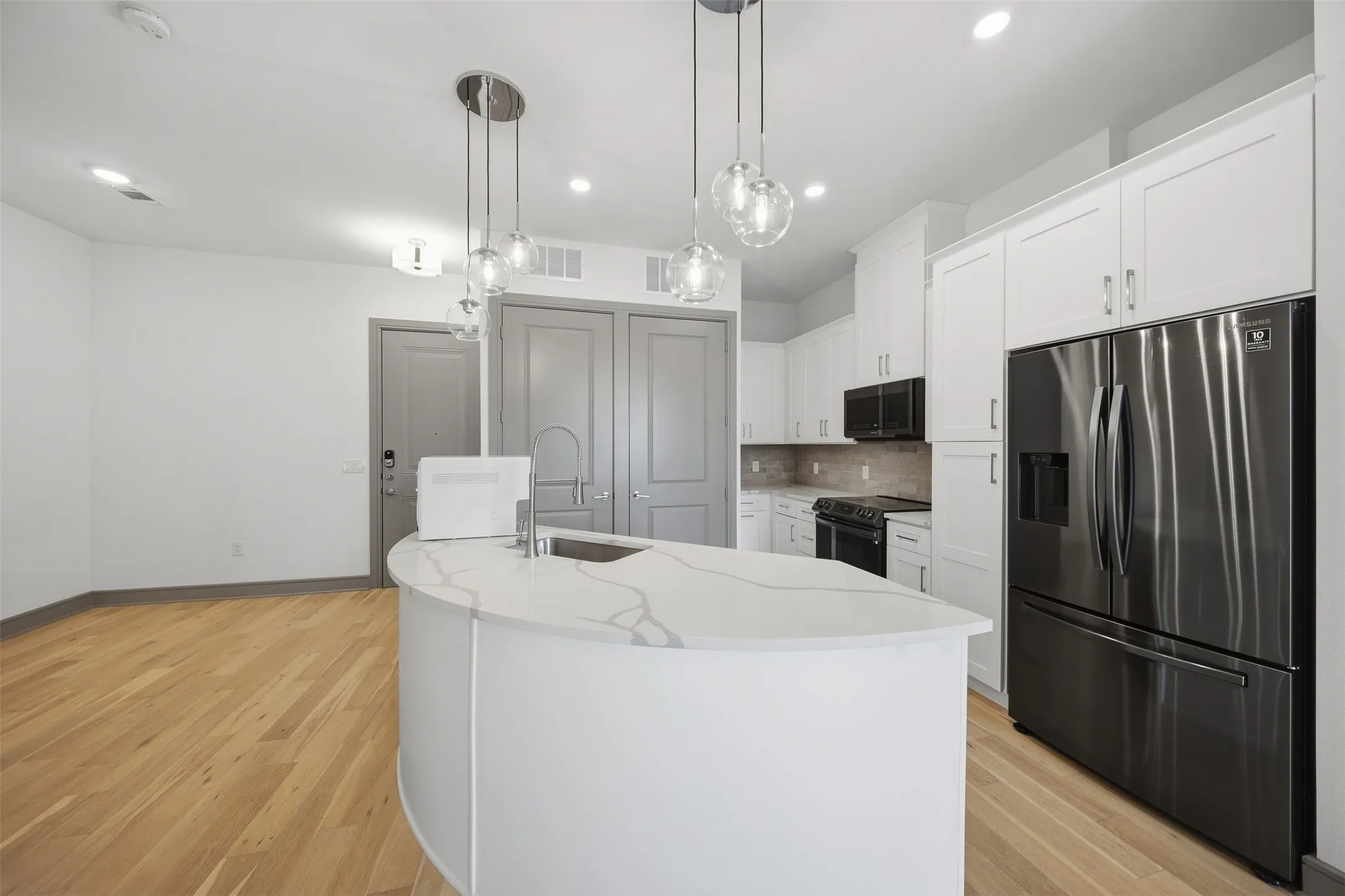 Kitchen featuring a curved island with integrated sink, white cabinetry, dark stainless steel appliances, and wood-finish flooring