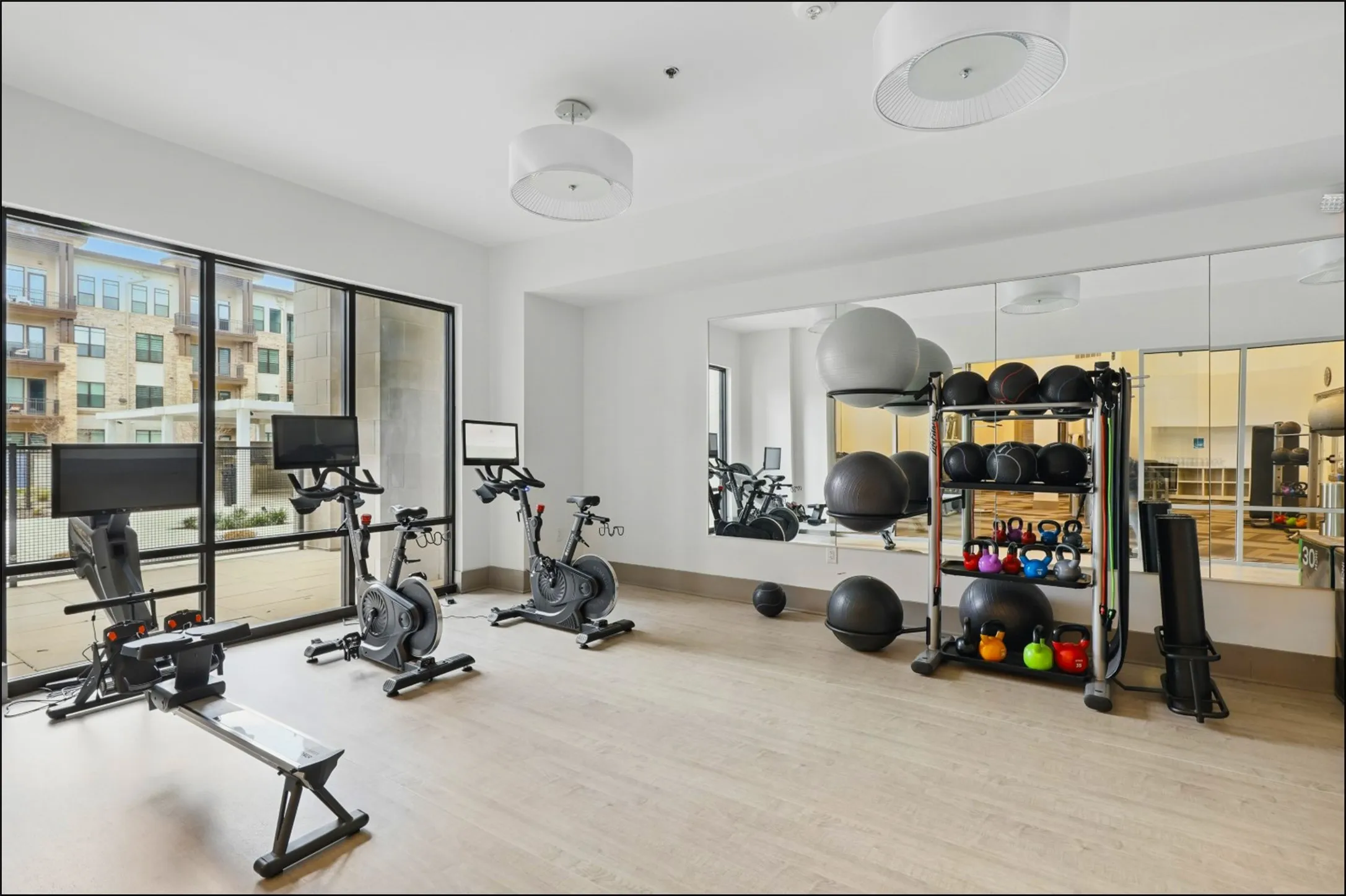 Fitness center featuring floor-to-ceiling windows, light wood-finish flooring, full-length wall mirrors, and recessed lighting