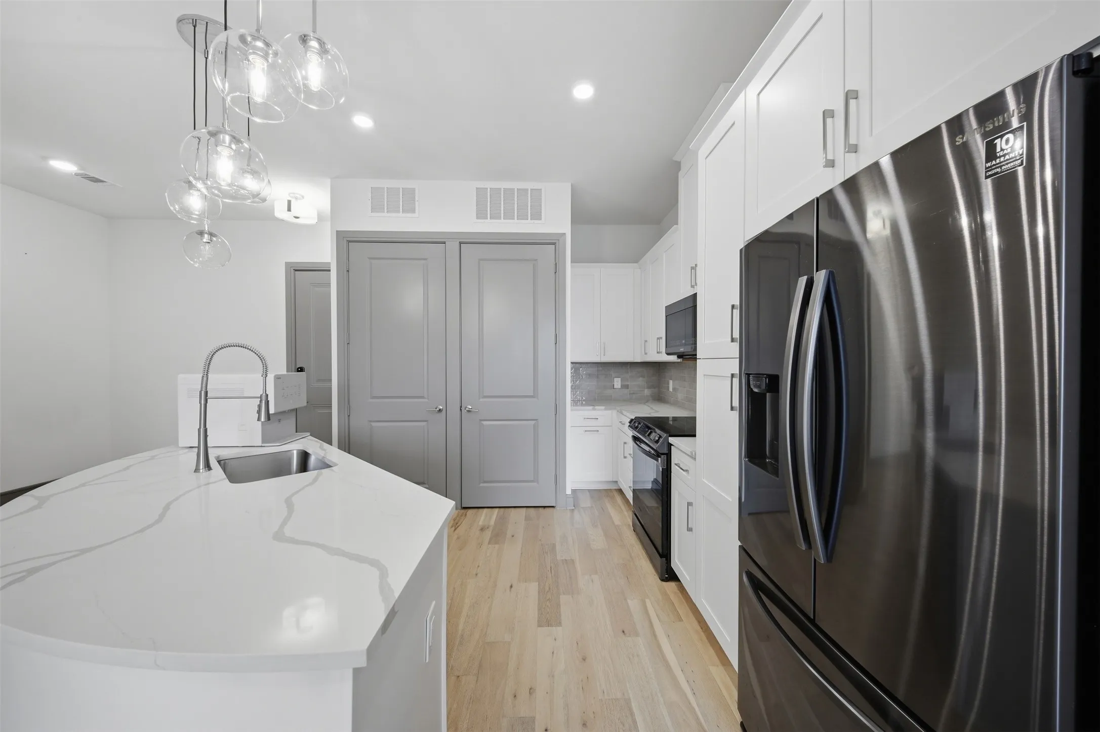Kitchen featuring a spacious island with an undermount sink, white cabinetry, dark-finished appliances, light wood-finish flooring, and pendant lighting