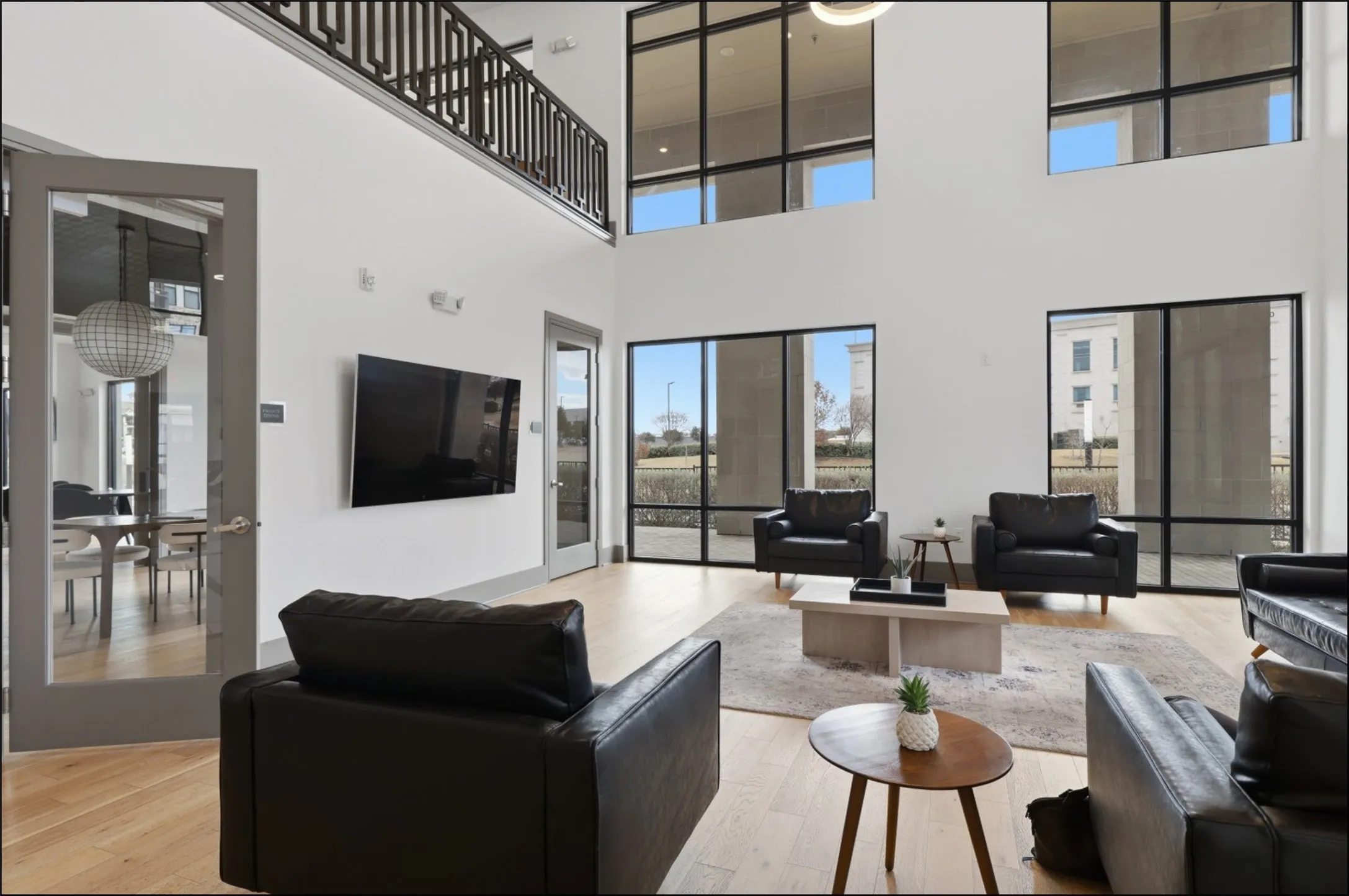 High ceilings, wood-finish flooring, full-height windows, a glass-paneled door, and an upper-level overlook with a decorative railing
