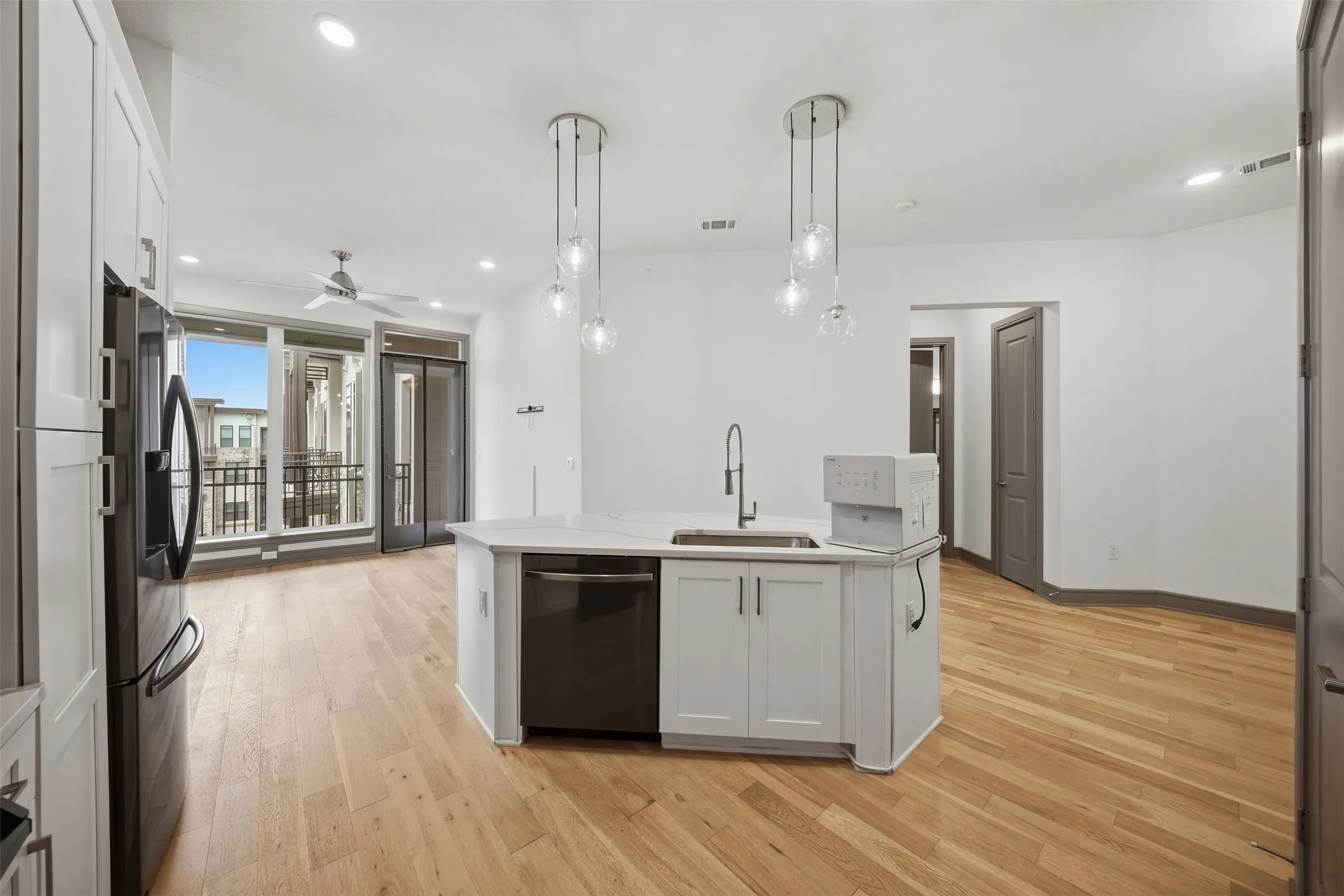 Open-concept living area featuring wood-finish flooring, a kitchen island with a sink and pendant lighting, and a private balcony