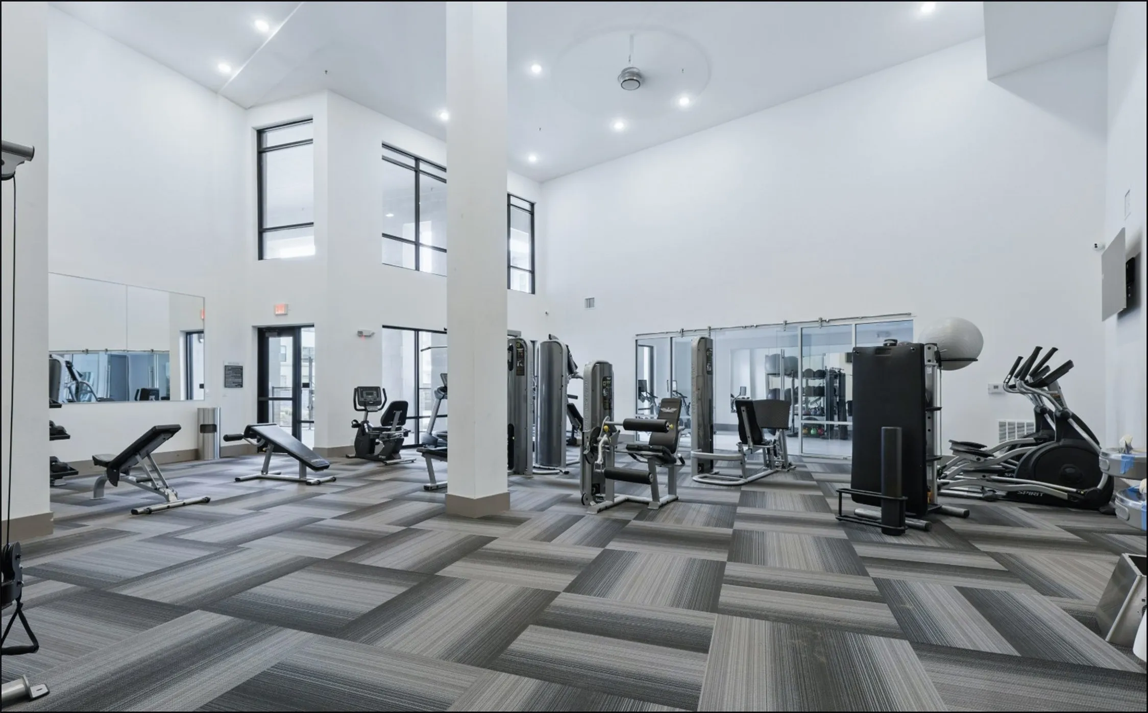 Fitness center featuring high ceilings, patterned carpet flooring, extensive natural light through large windows, and a variety of exercise equipment