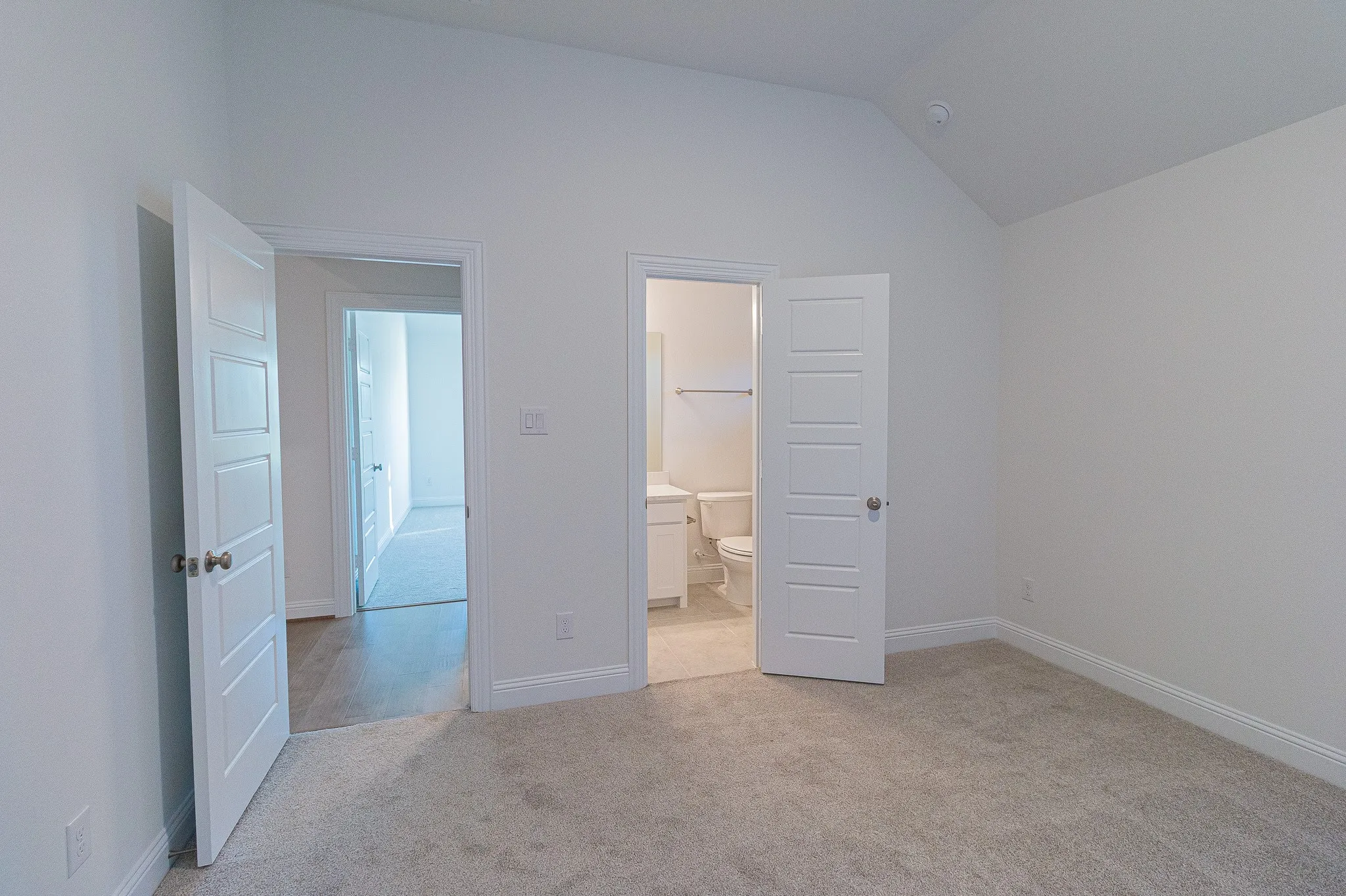 Unfurnished bedroom with light colored carpet, lofted ceiling, and ensuite bathroom