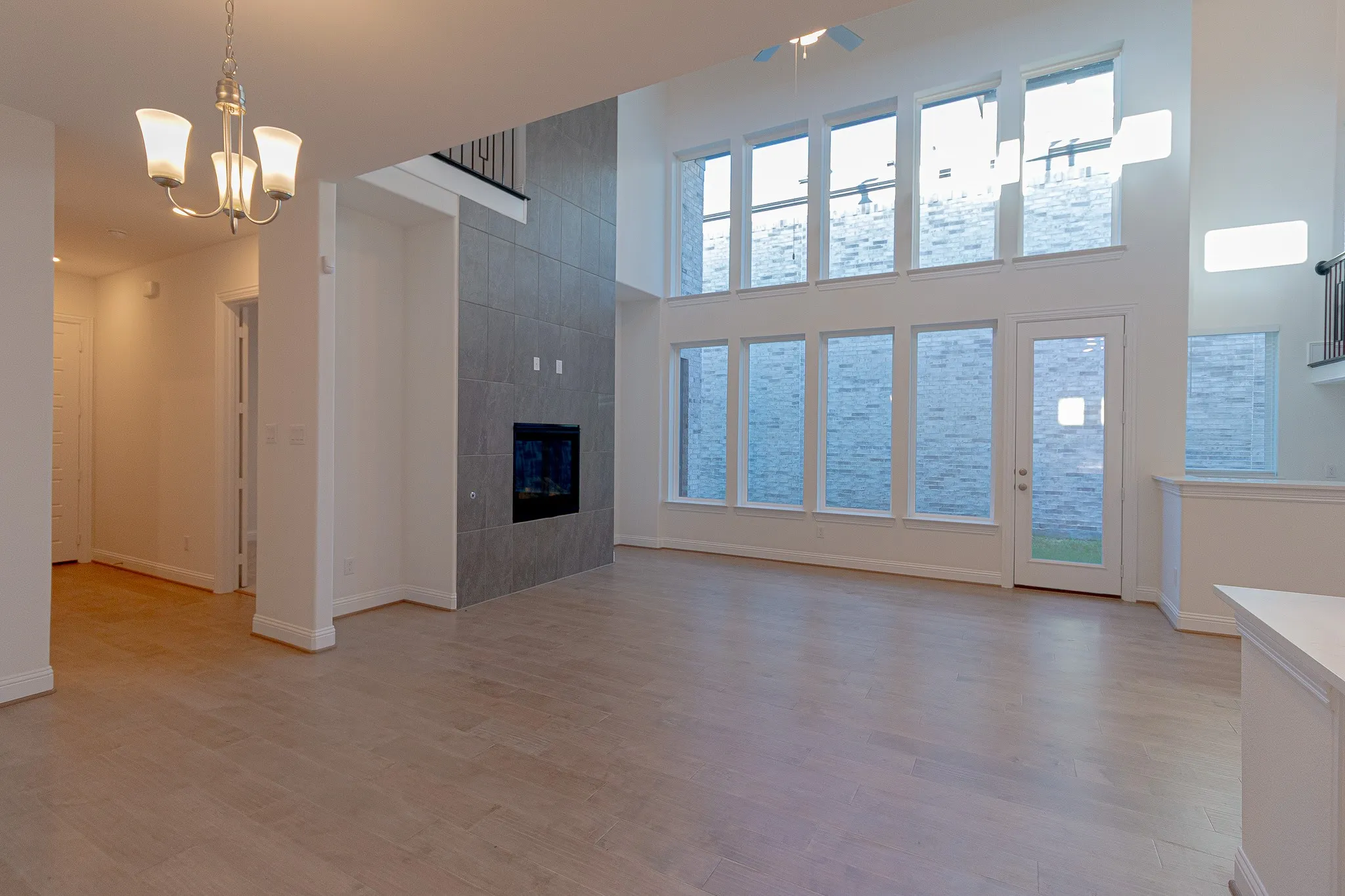 Unfurnished living room featuring a high ceiling, light wood-style flooring, a chandelier, a fireplace, and ceiling fan