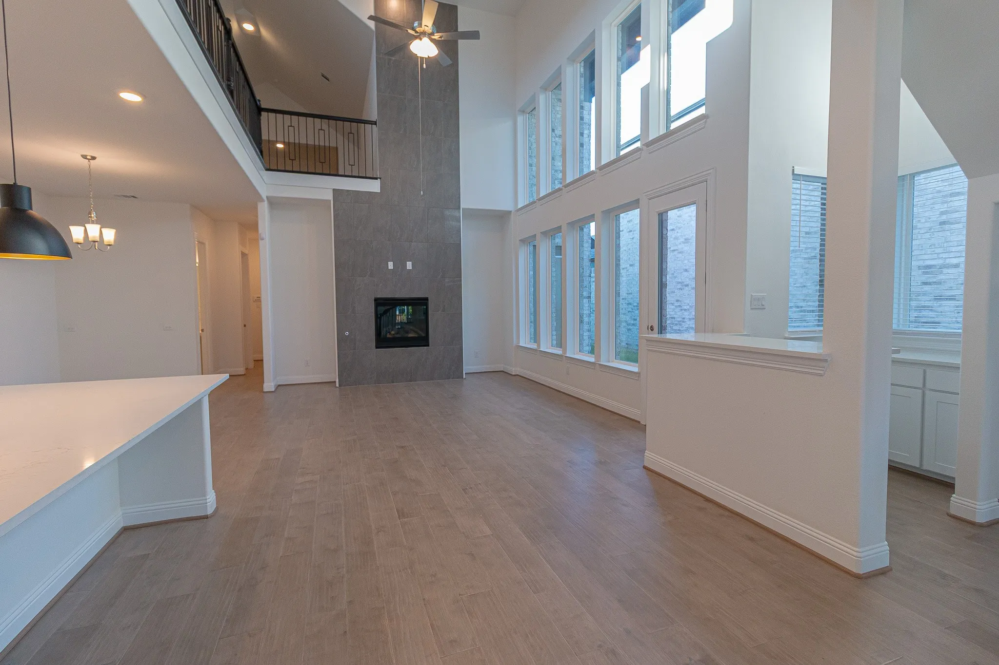 Unfurnished living room featuring a towering ceiling, ceiling fan, healthy amount of natural light, light wood-type flooring, and recessed lighting