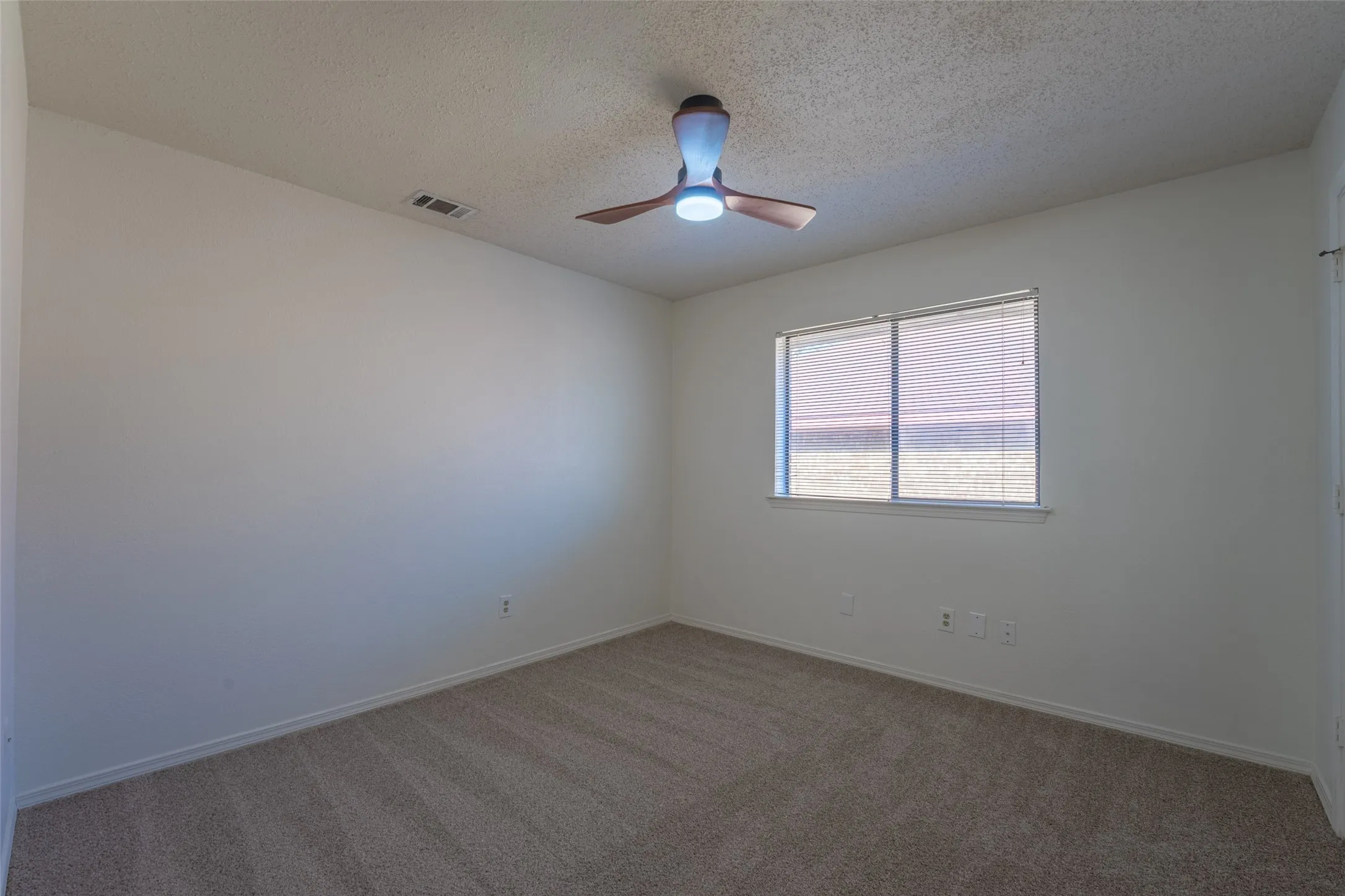 Neutral wall paint, textured ceiling, window with blinds, ceiling fan with integrated lighting, and carpet flooring