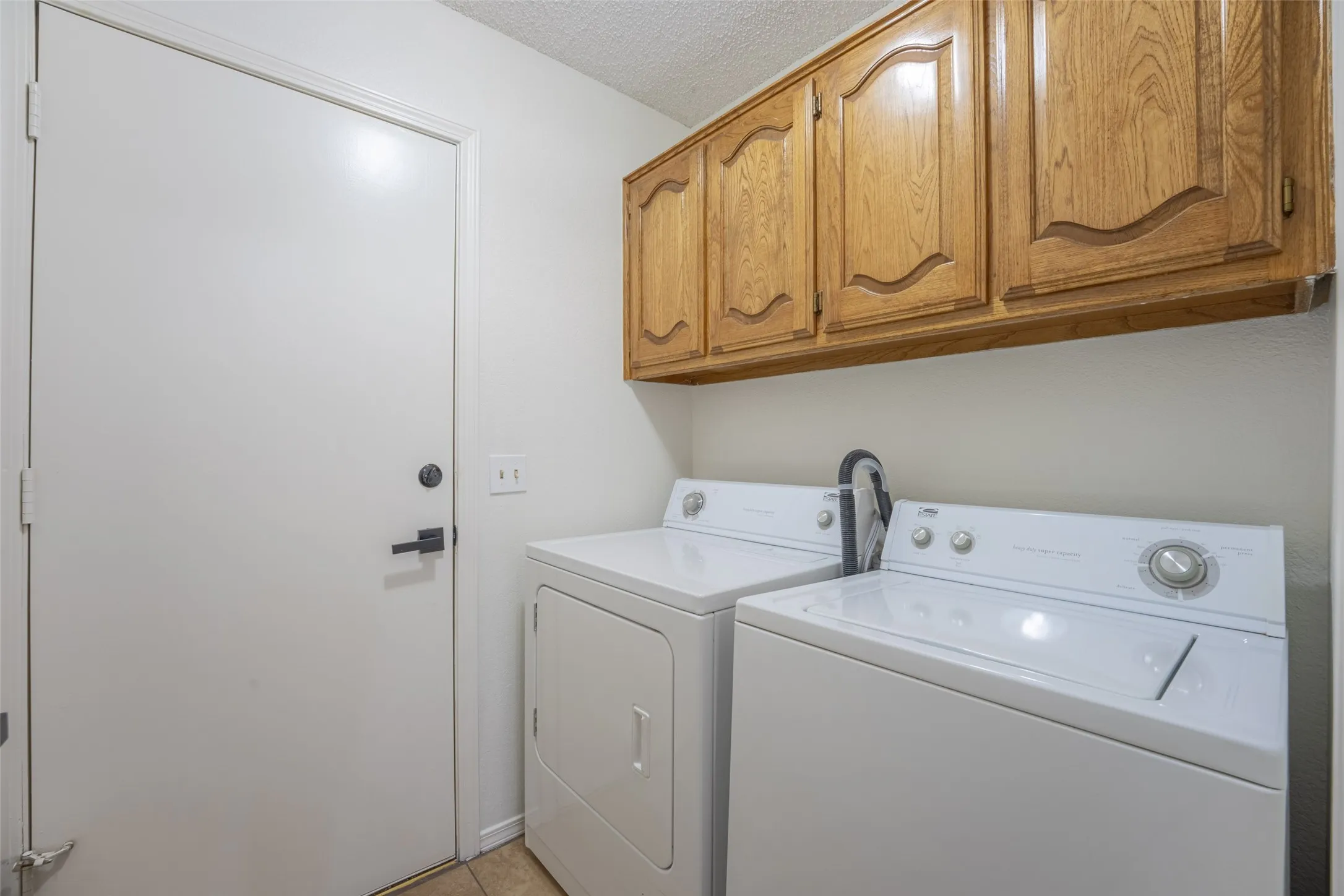 Laundry area featuring wood-finish cabinetry, tile flooring, and a solid core door