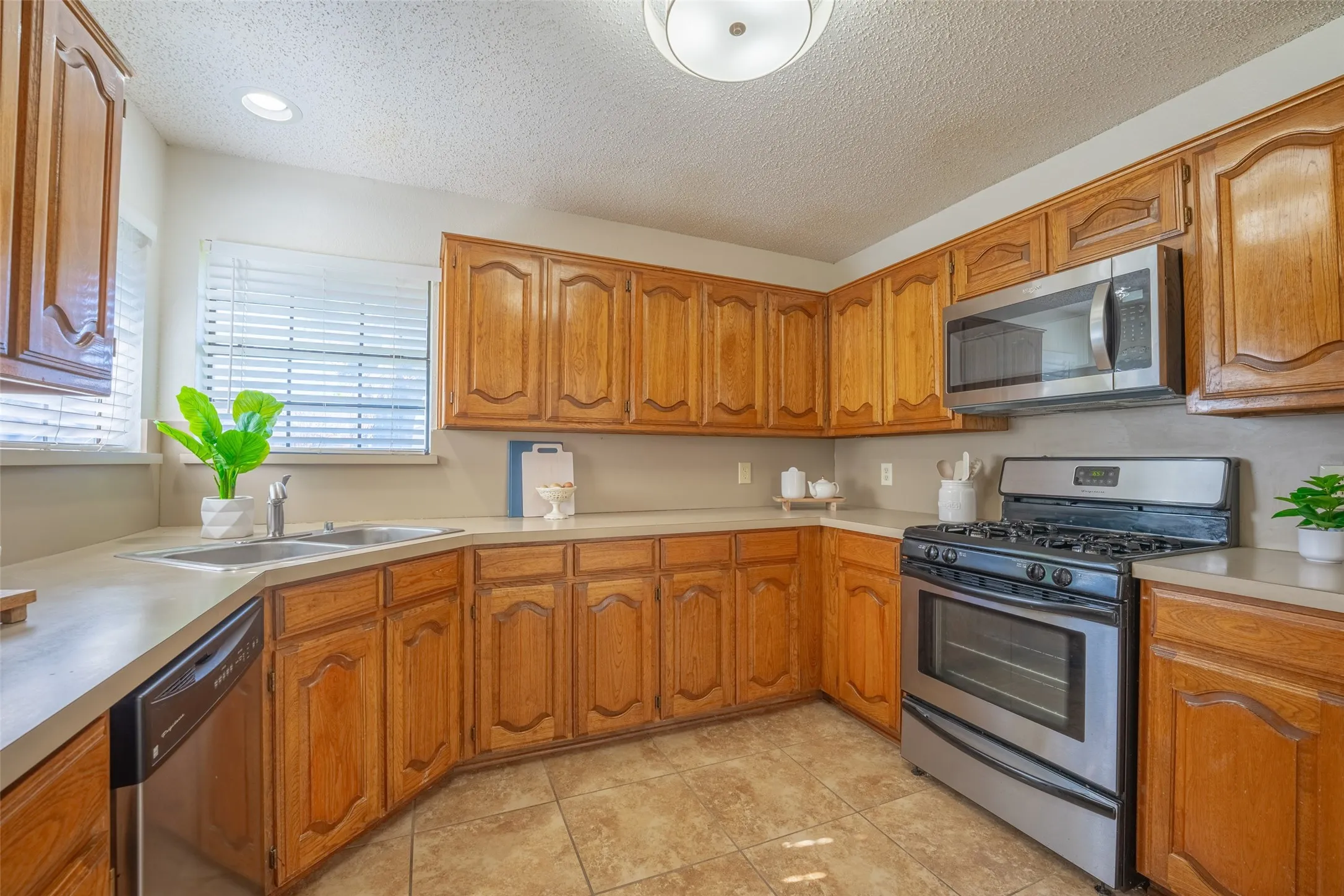 Wood-finish cabinetry, stainless steel appliances, dual basin sink, integrated dishwasher, and tiled flooring