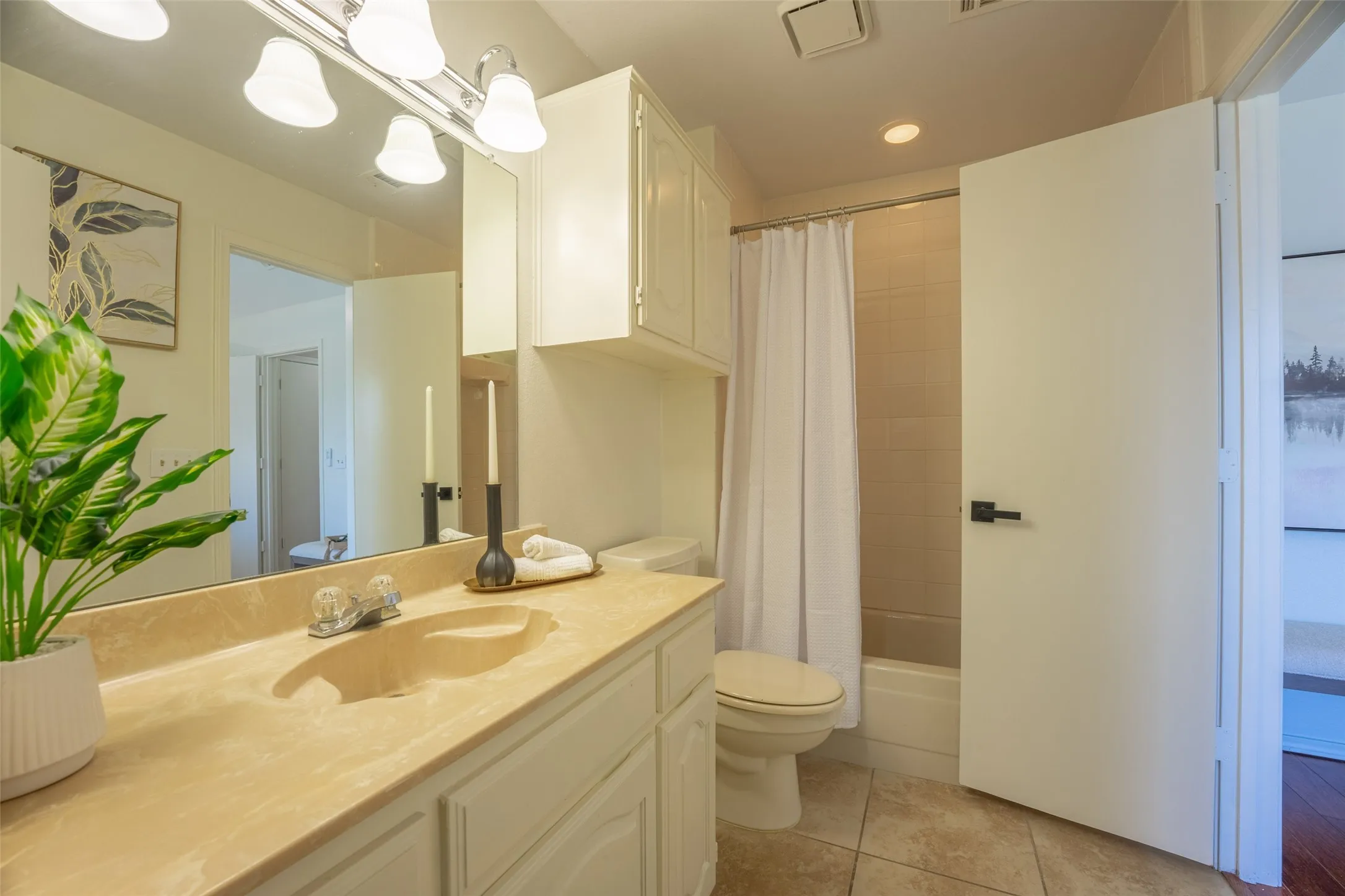 Bathroom featuring a full vanity with an integrated sink, overhead wall-mounted cabinetry, a shower-tub combination, and tiled flooring