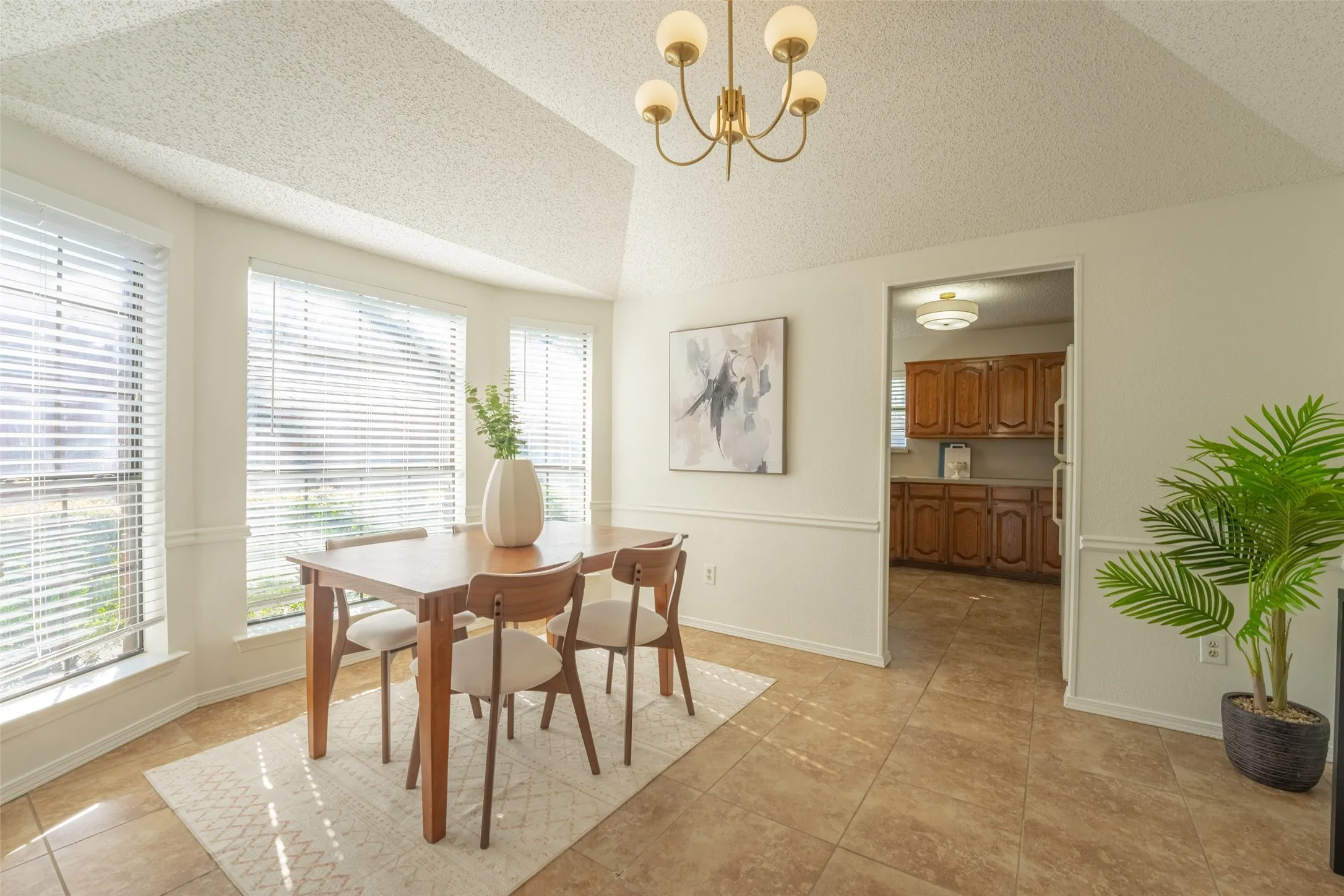 Bay window with horizontal blinds, tiled flooring, vaulted ceiling, and brass-finish chandelier