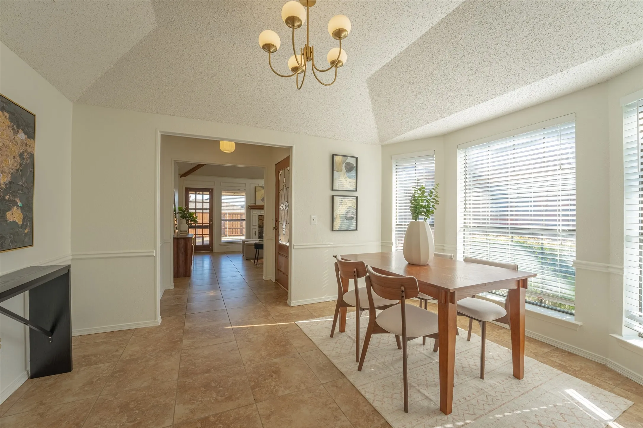 Vaulted ceiling, ceramic tile flooring, chair rail molding, bay window with blinds, and decorative chandelier