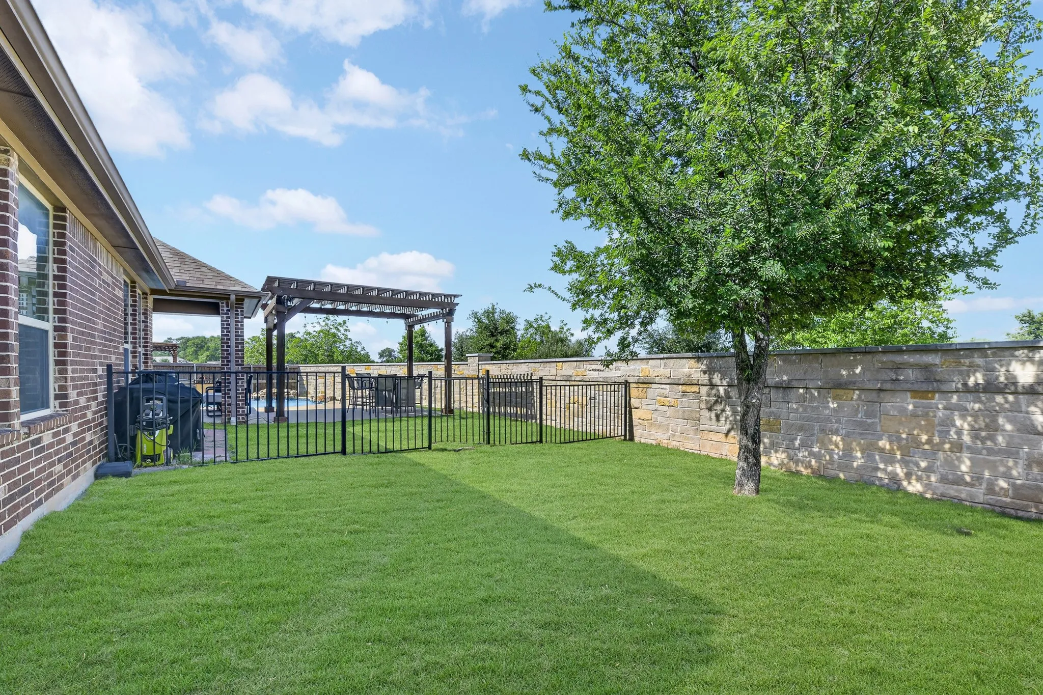 Expansive lawn area featuring a mature tree, stone perimeter wall, and black metal fencing
