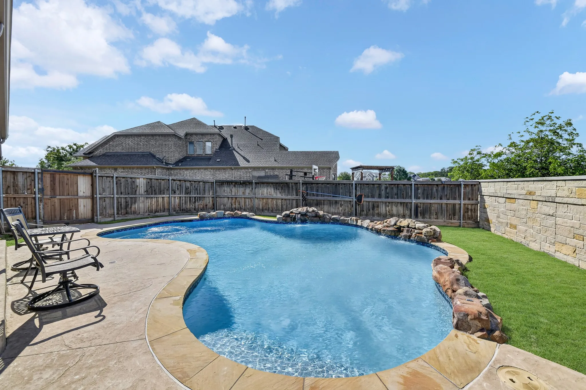 Curved swimming pool with rock waterfall features, surrounded by stamped concrete decking and a manicured lawn