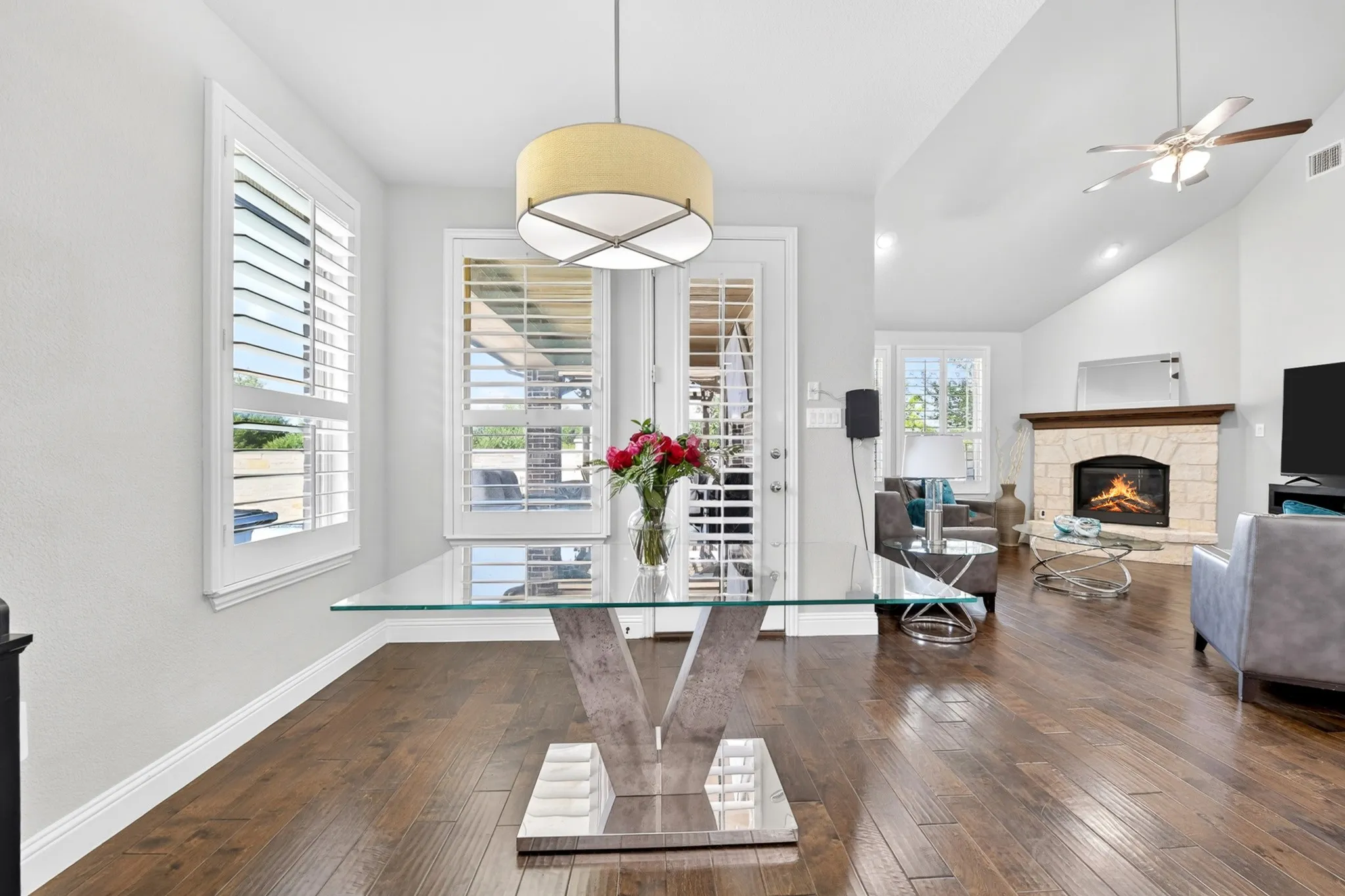 Hardwood flooring throughout, white plantation shutters, vaulted ceiling, and a stone-faced fireplace