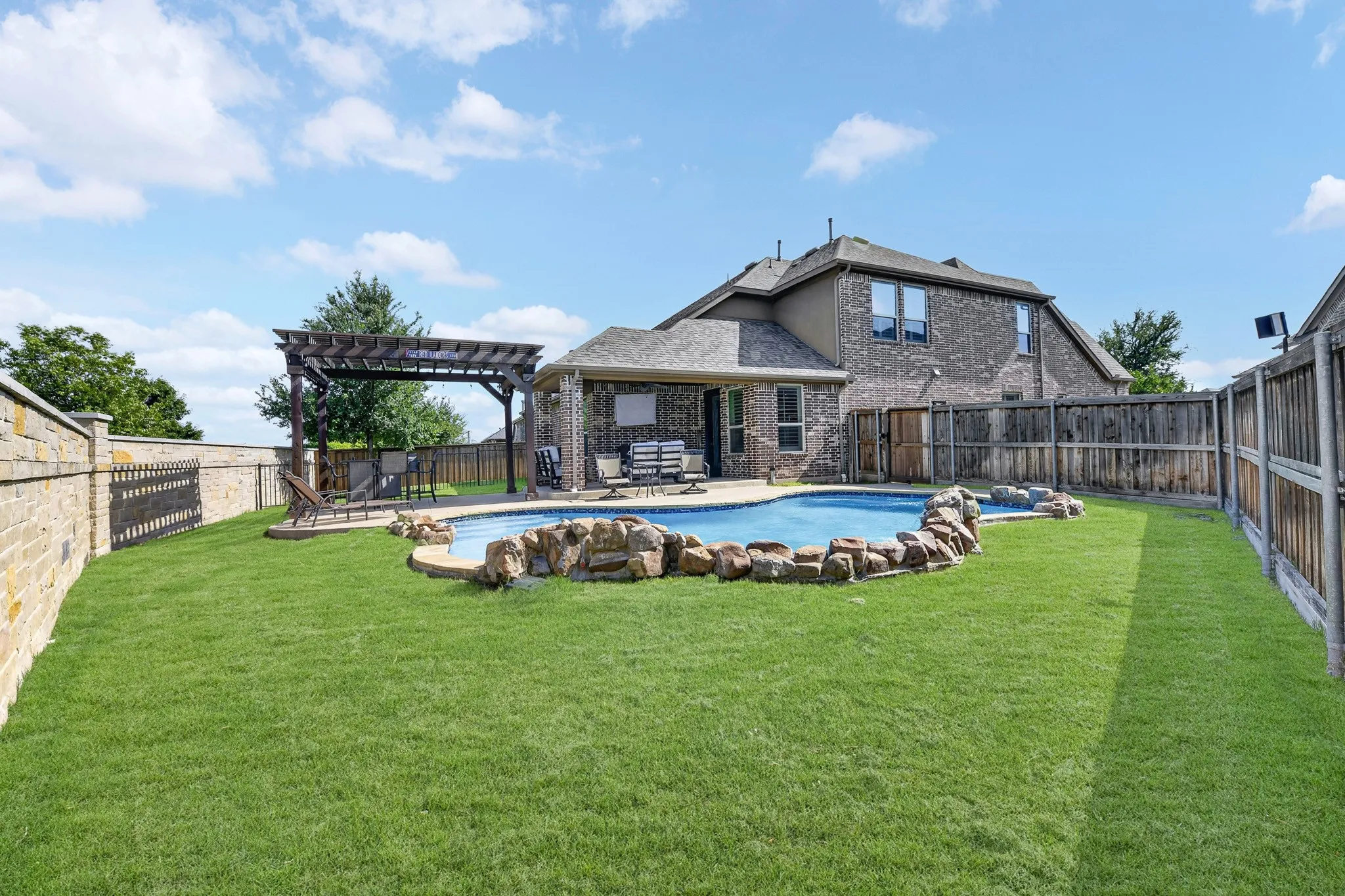 Expansive backyard featuring a large swimming pool with rock detailing, a covered patio, and a wood pergola