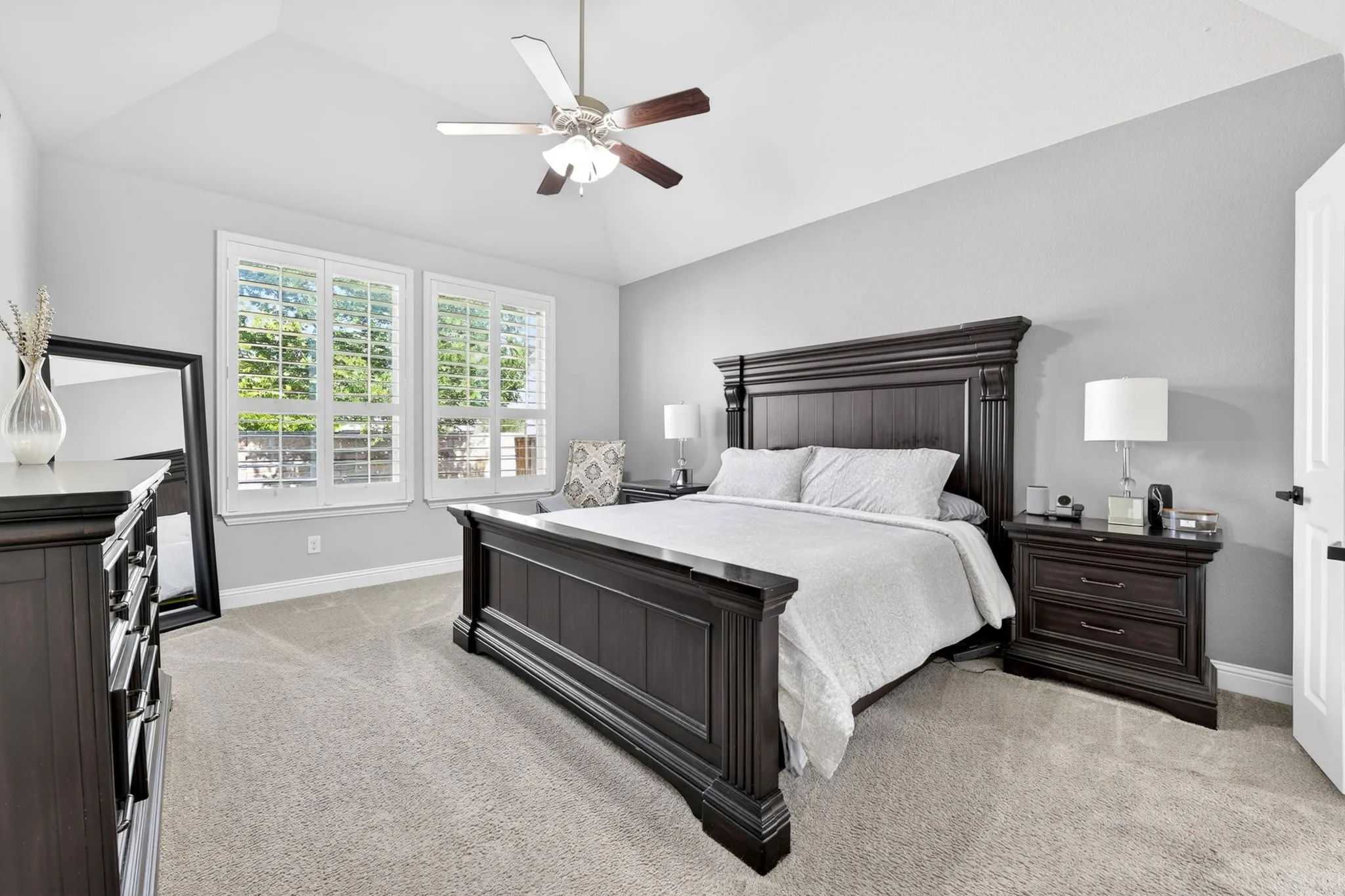 Vaulted ceiling with a ceiling fan, dual windows with plantation shutters, and light-toned carpeting