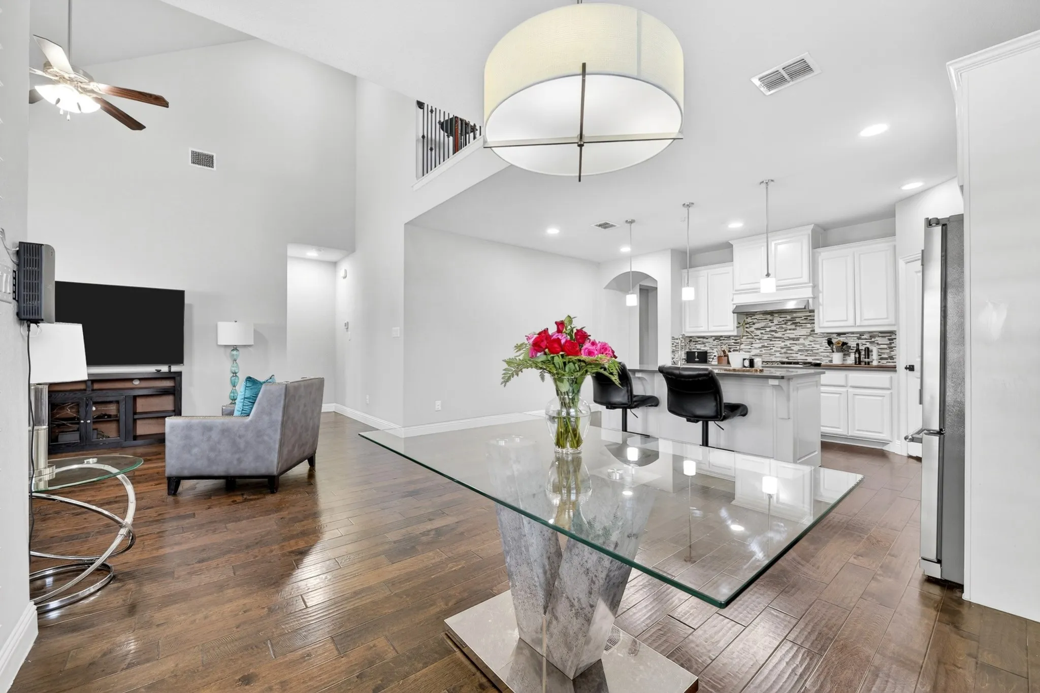 Open concept living area featuring wood-finish flooring, vaulted ceilings, and a kitchen with white cabinetry and a tile backsplash