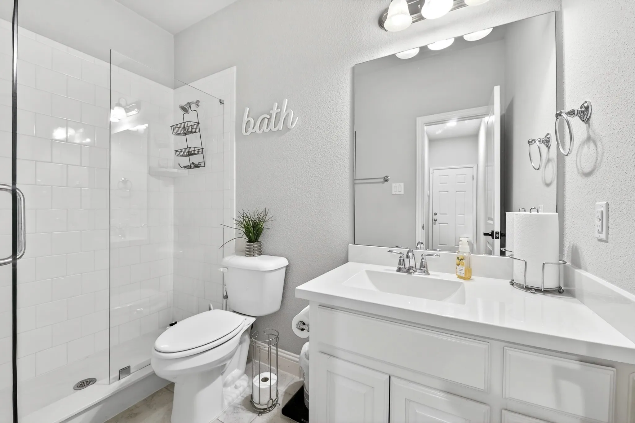 Glass-enclosed shower with subway tile surround, white vanity with integrated sink, polished chrome faucet, and overhead vanity lighting