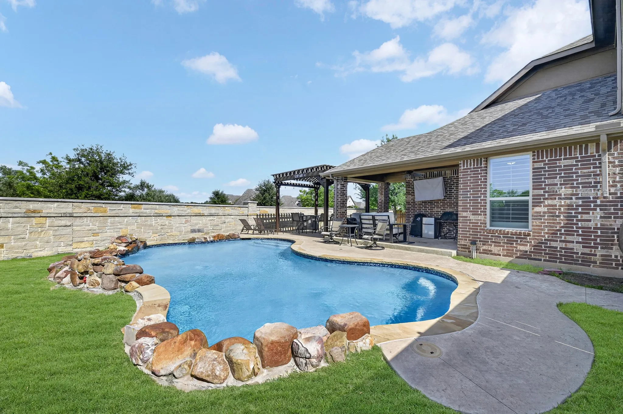 Freeform swimming pool with rock surround, extended patio, and covered outdoor living space