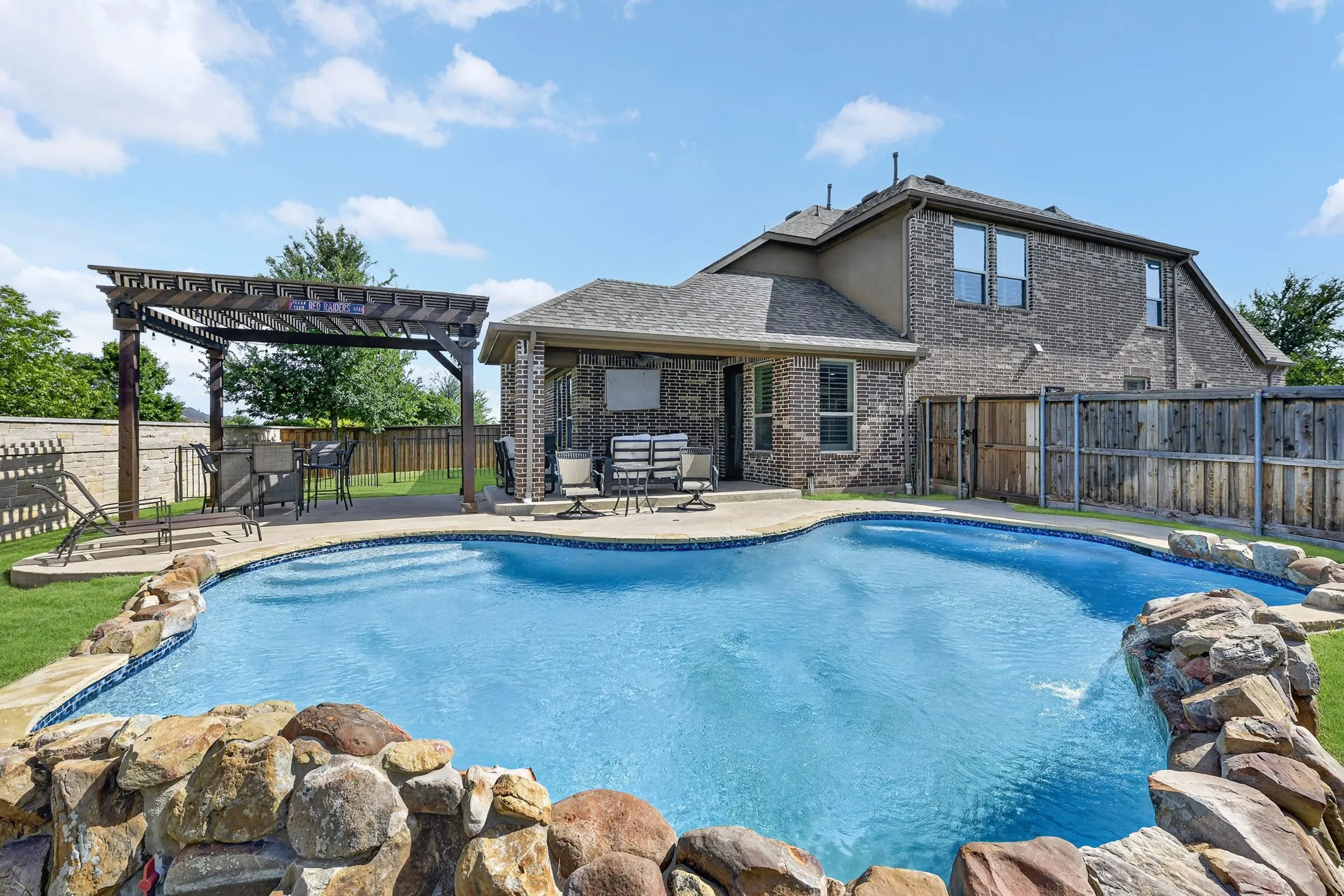 Resort-style backyard featuring a custom-shaped swimming pool with rock detailing and a waterfall