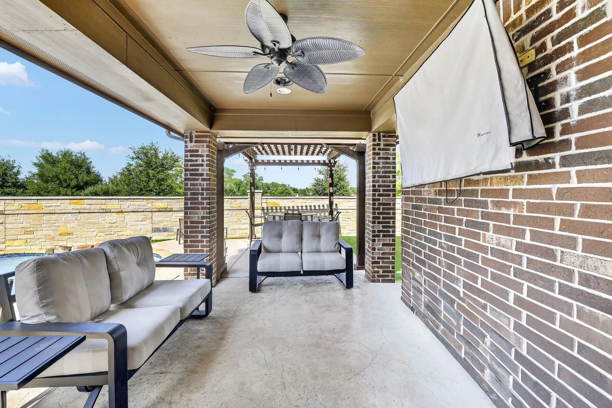 Covered patio with a ceiling fan, brick accent wall, and concrete flooring
