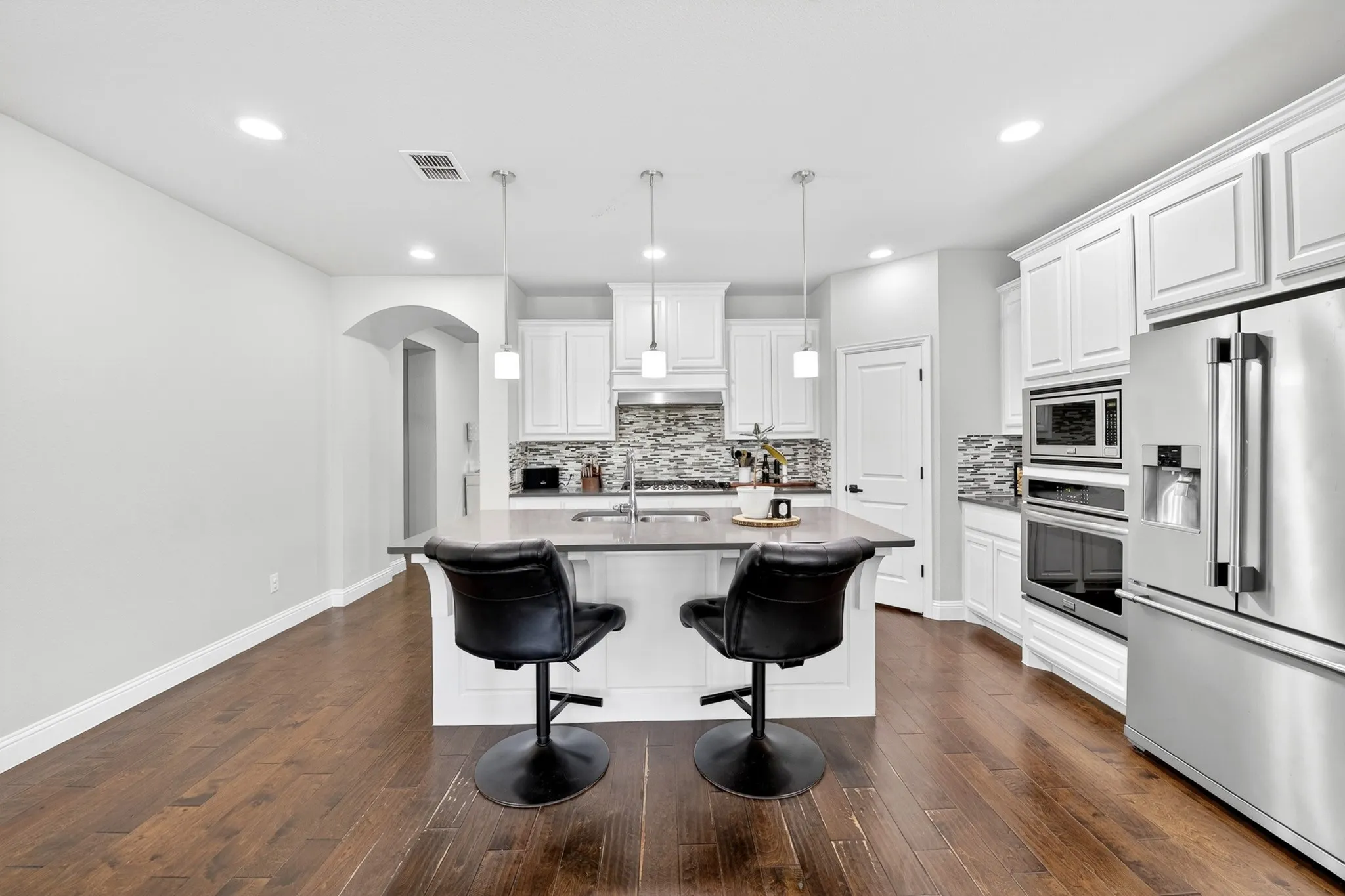 Kitchen featuring wood-finish flooring, a central island with countertop, white cabinetry, integrated stainless steel appliances, and a tiled backsplash