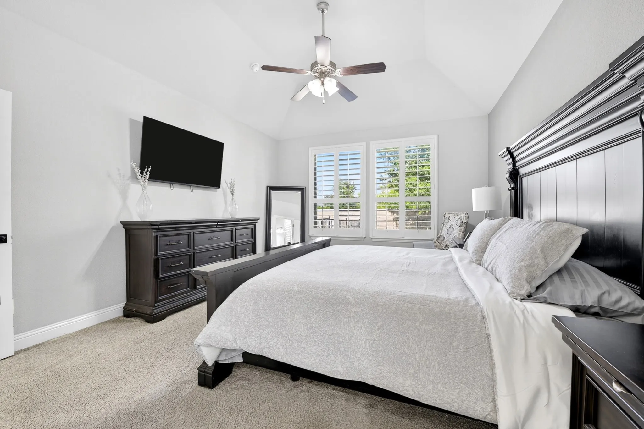 Vaulted ceiling, ceiling fan, carpeted flooring, window with plantation shutters, and a wall-mounted television