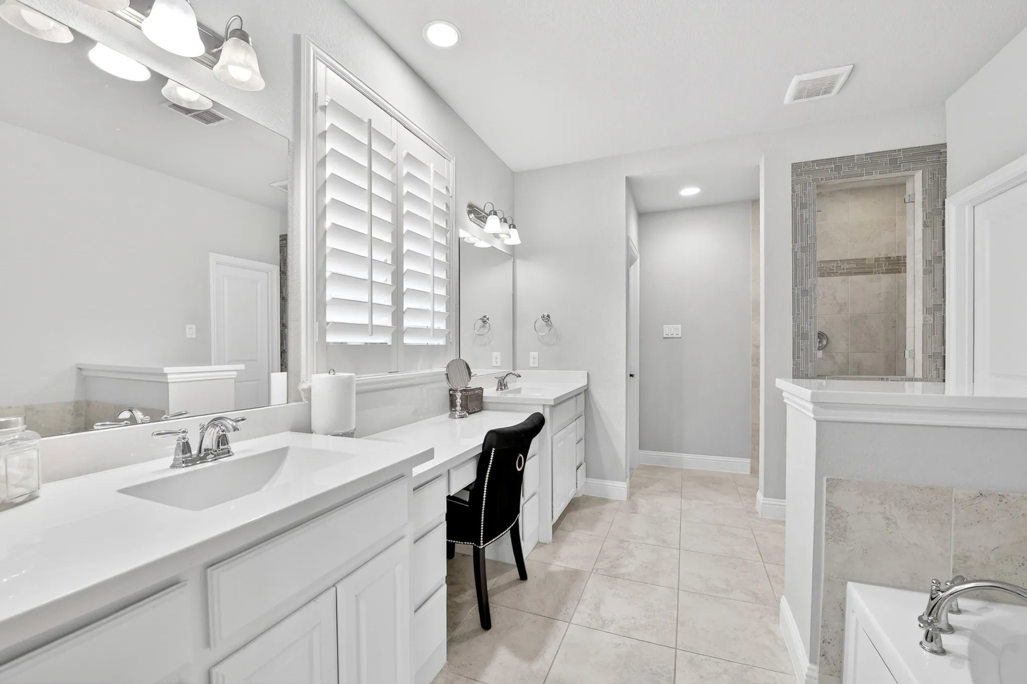 Dual vanity with integrated sinks, light-toned tiled flooring, white plantation shutters, built-in shower, and a built-in tub