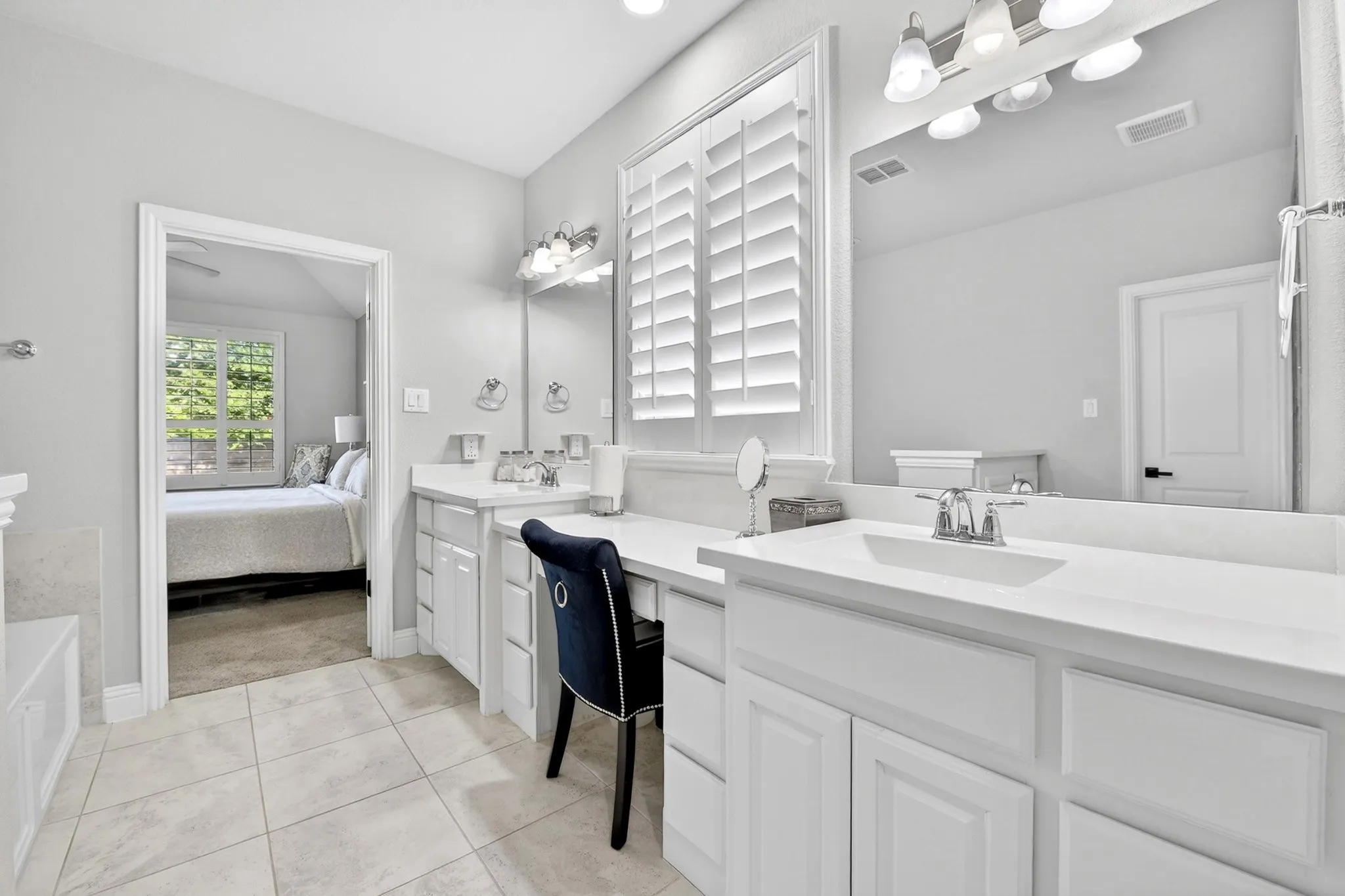 Dual vanities with integrated sinks, white cabinetry, a built-in vanity area, a large mirror, and tile flooring