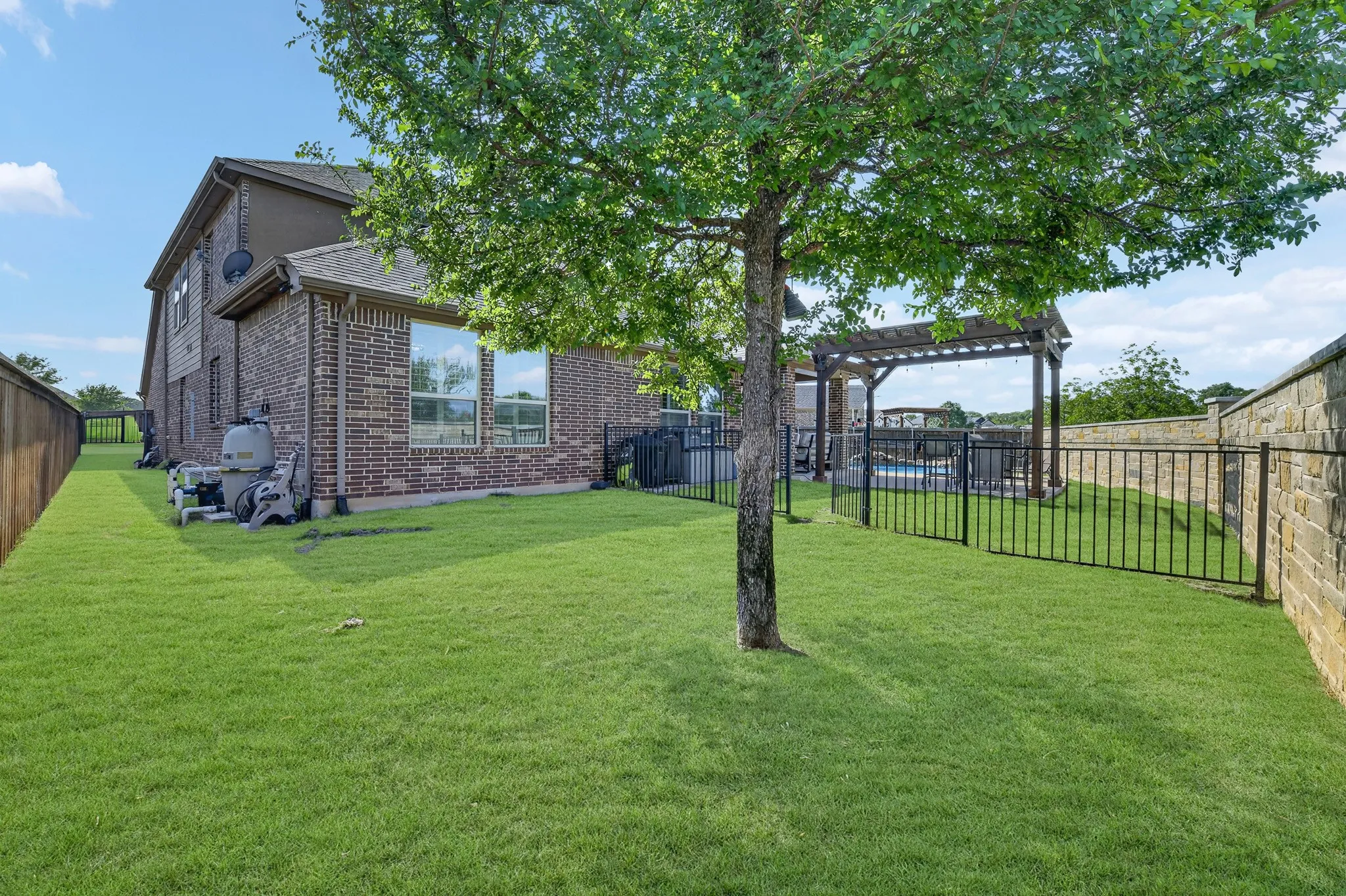 Expansive lawn with mature trees, brick exterior, and a privacy fence