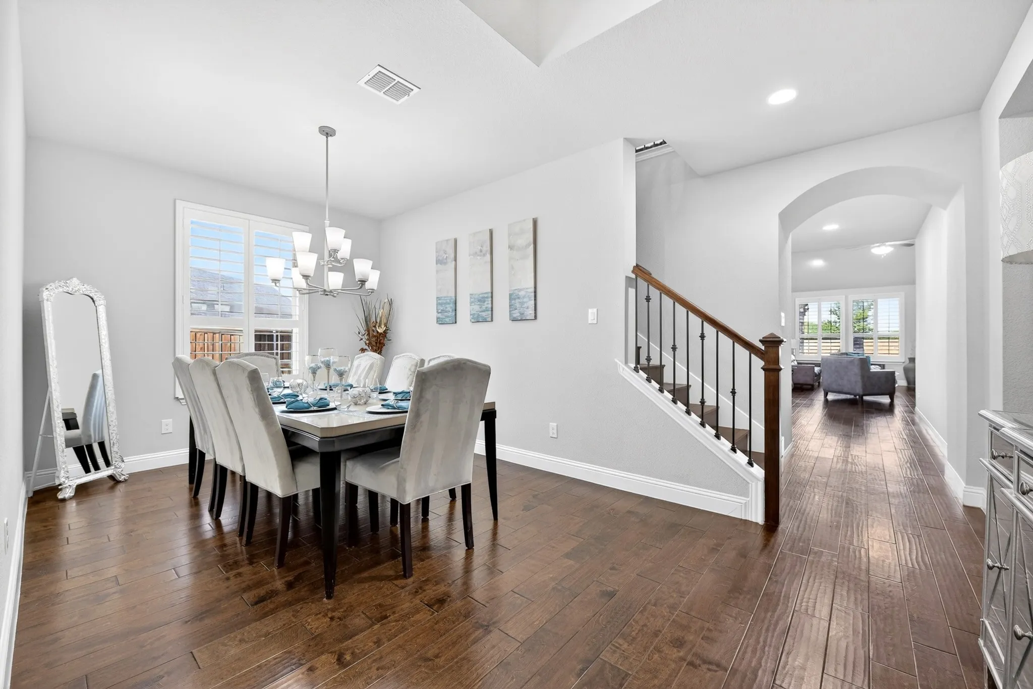 Wood-finish flooring throughout, a modern chandelier, and a staircase with dark wood handrails and black metal balusters