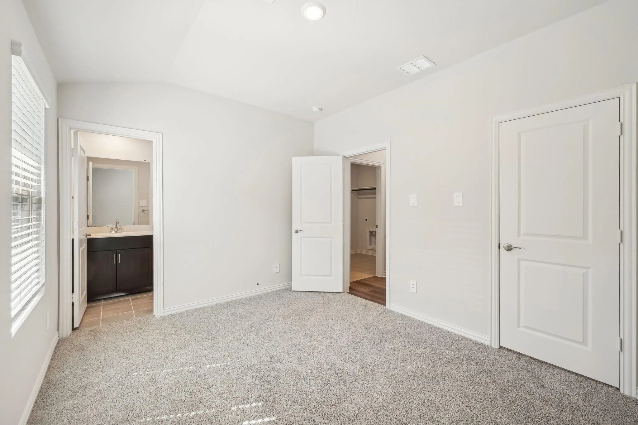 Unfurnished bedroom featuring baseboards, light carpet, vaulted ceiling, and ensuite bath