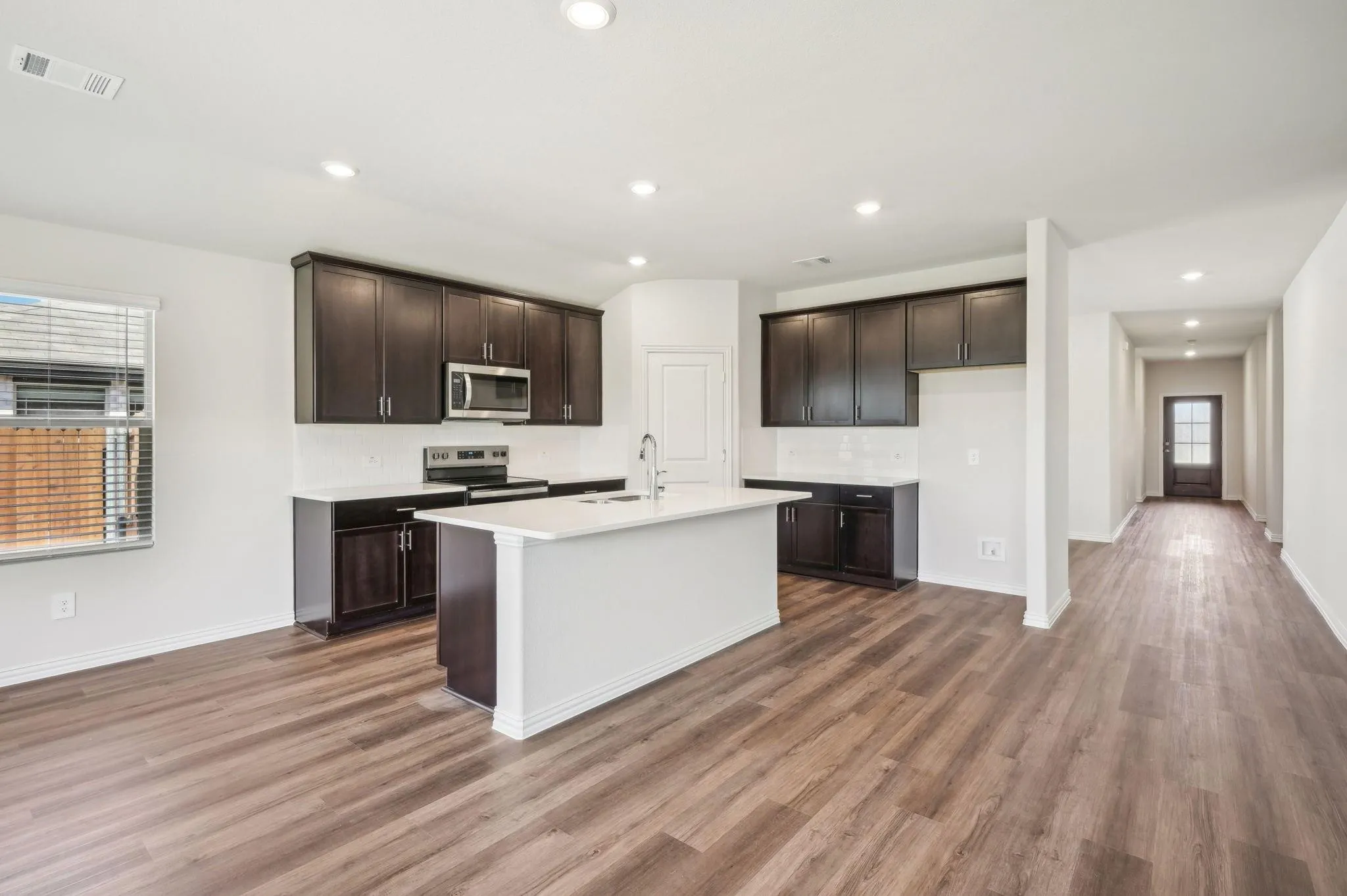 Kitchen featuring decorative backsplash, light wood-style flooring, appliances with stainless steel finishes, and dark brown cabinets