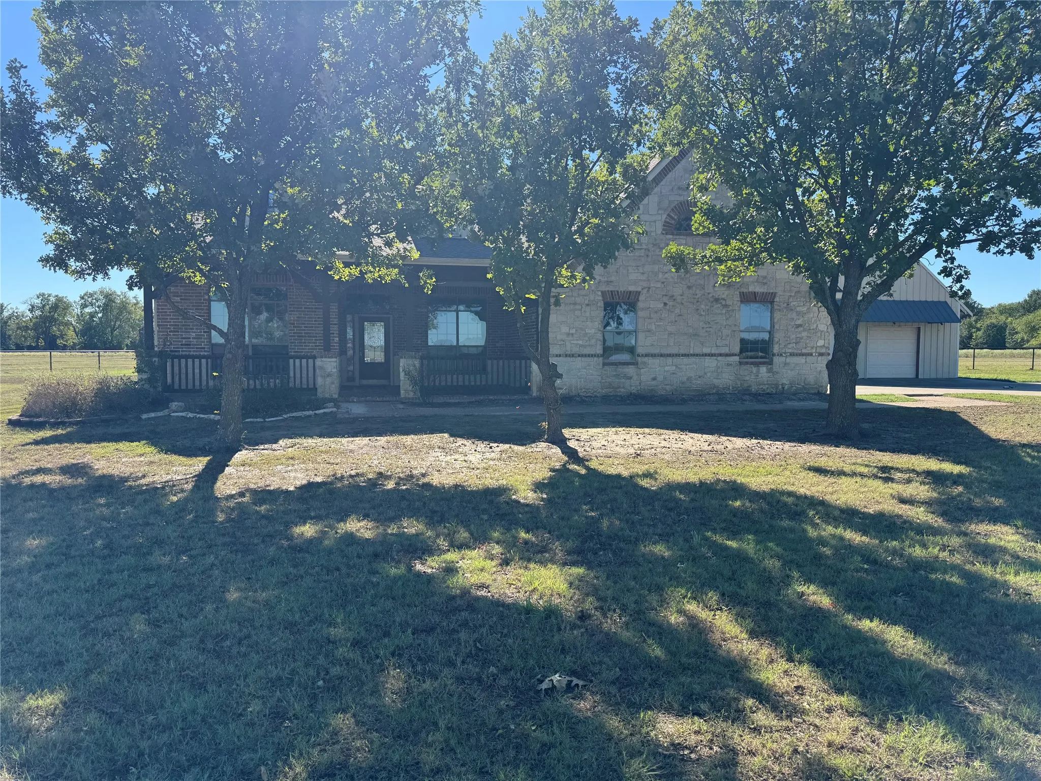 Brick and stone exterior with covered front porch, mature trees, and a detached structure featuring a metal roof
