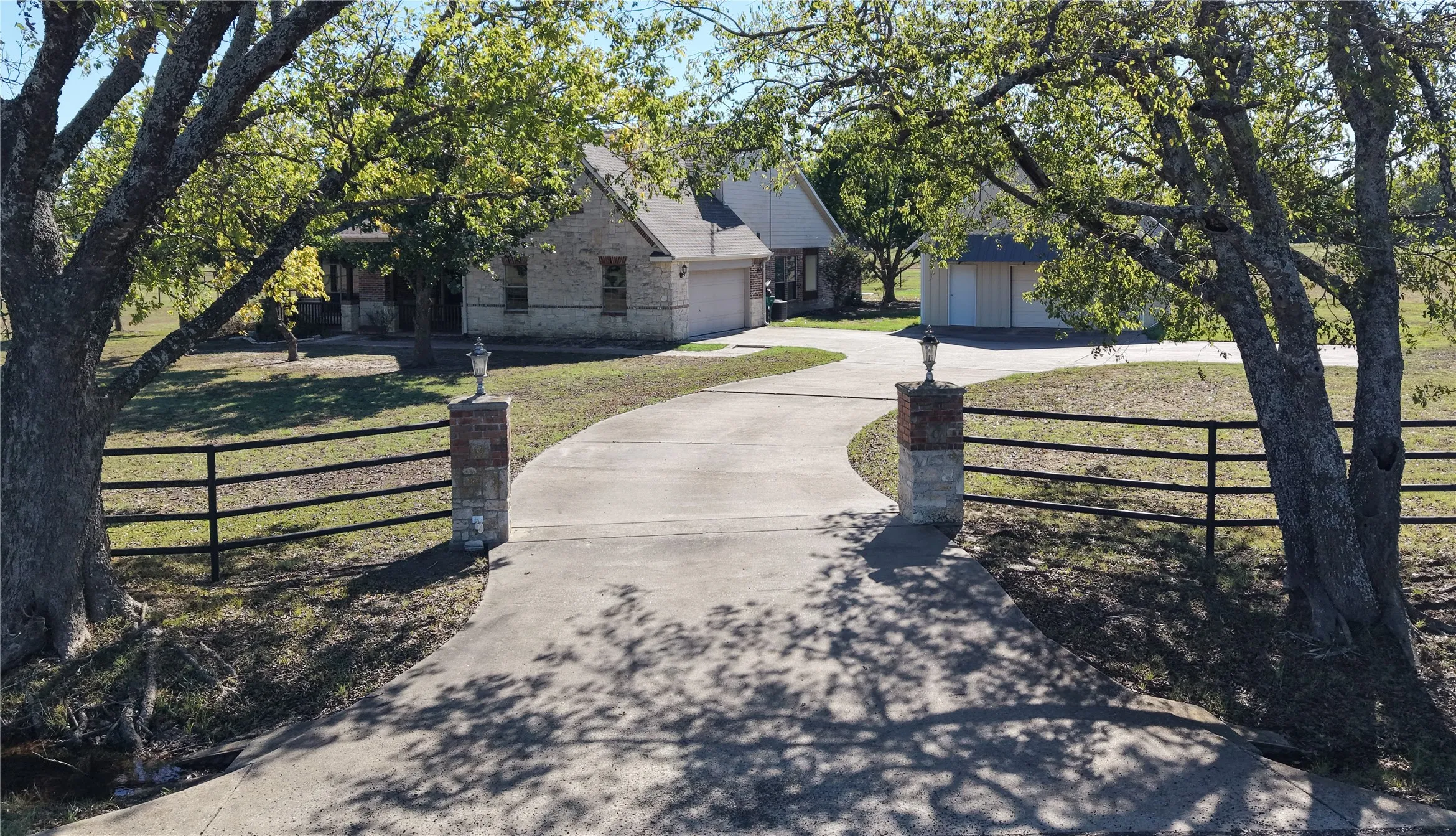 Stone facade home with an attached garage, featuring a paved driveway, decorative brick and stone pillars, and a black wrought iron fence