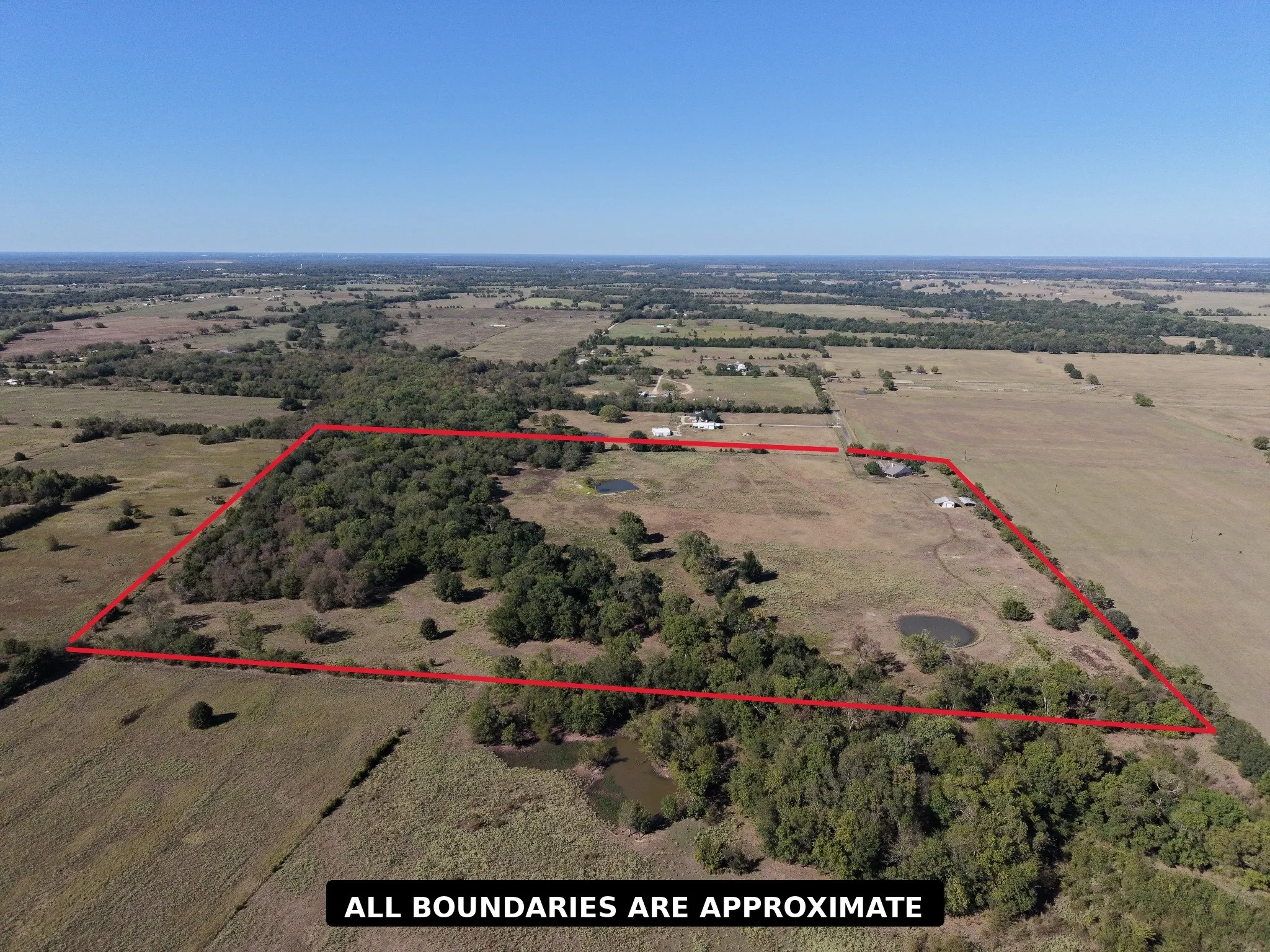Expansive rural property featuring a mix of open fields and mature tree cover, two visible ponds, and distant structures