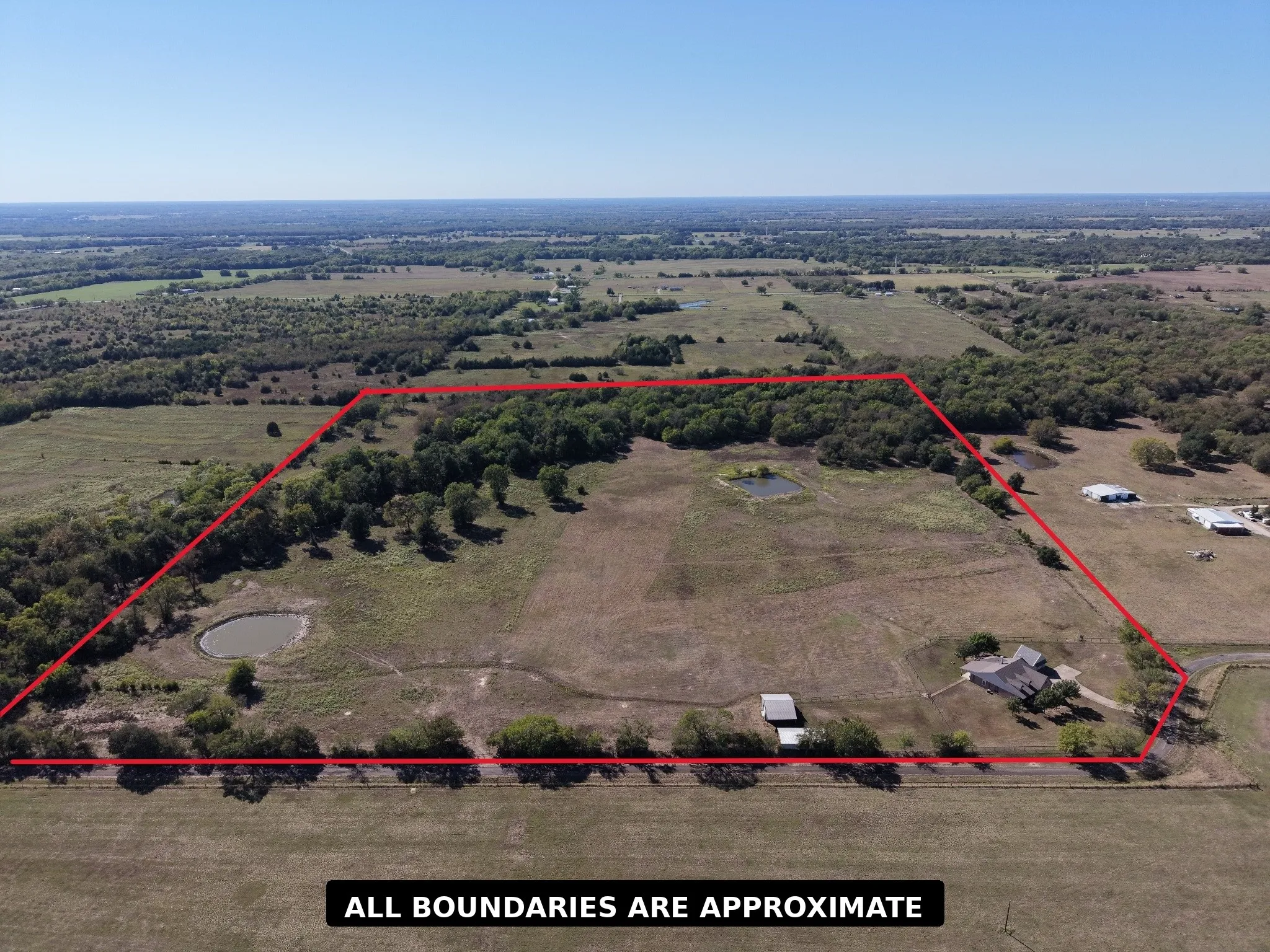 Expansive acreage featuring multiple ponds, mature trees, a single-story residence, and an accessory building