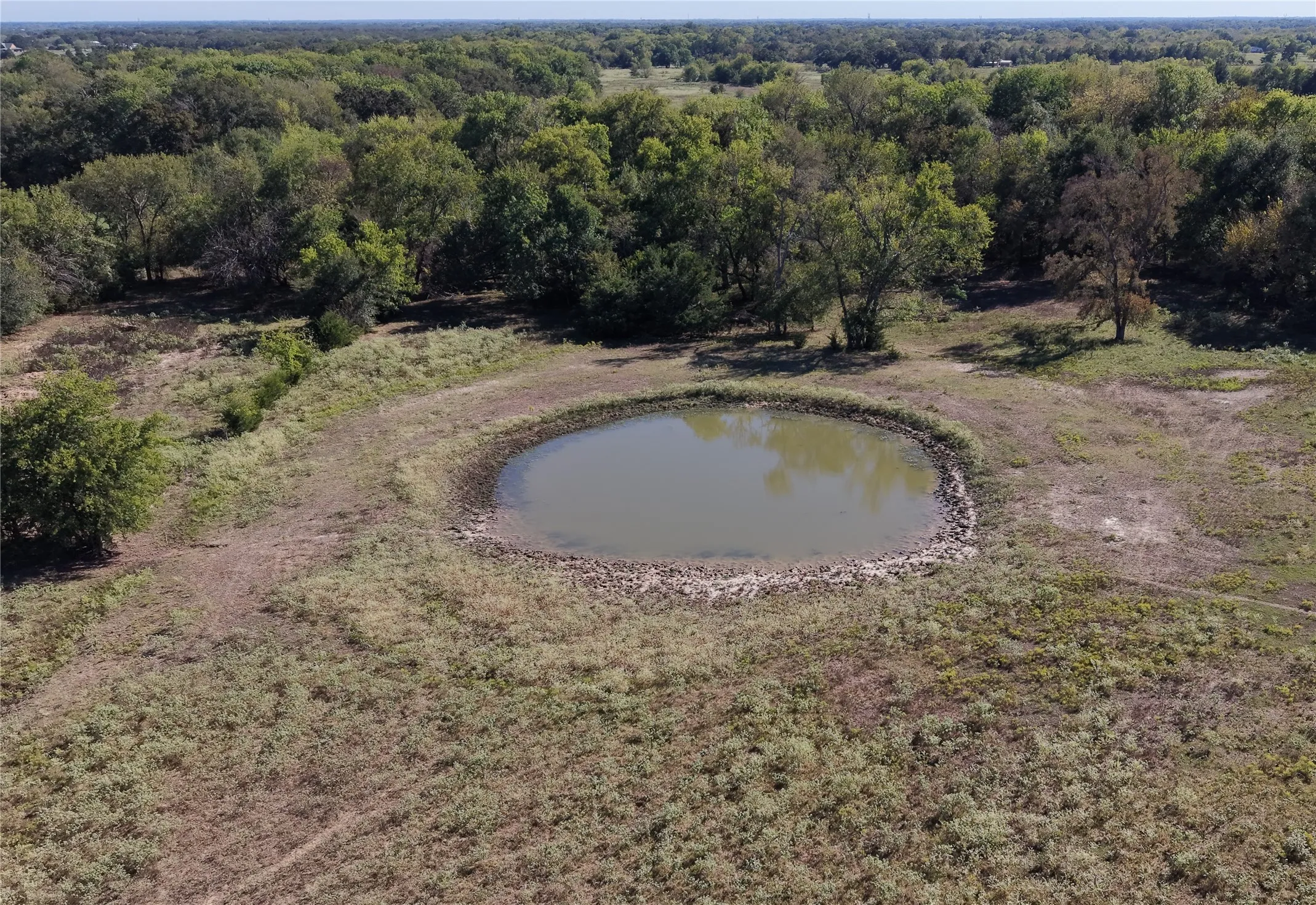 Natural pond feature with a rock-lined bank, surrounded by open land and mature trees