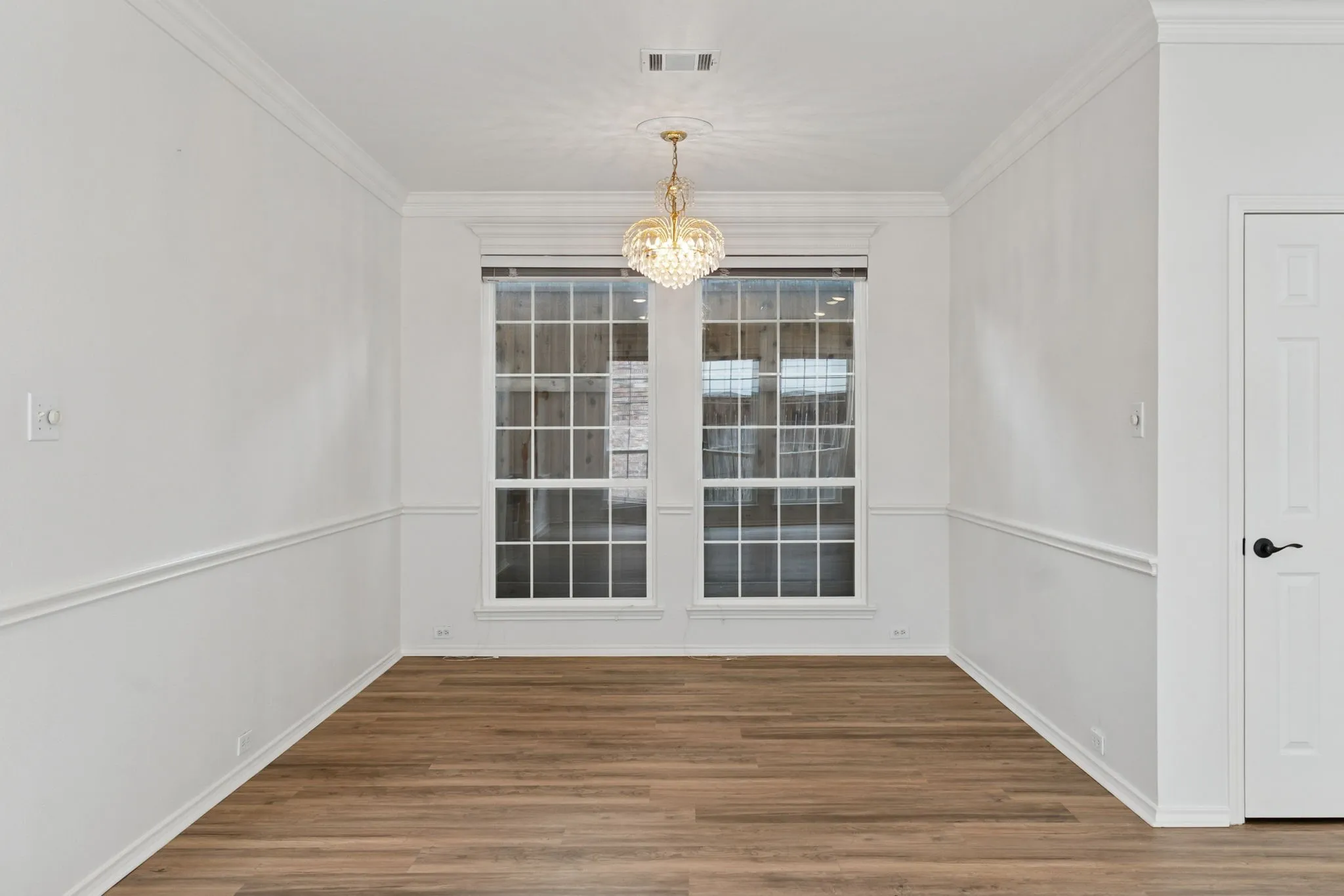 Wood-finish flooring, crown molding, chair rail molding, clear paned windows, and a decorative chandelier