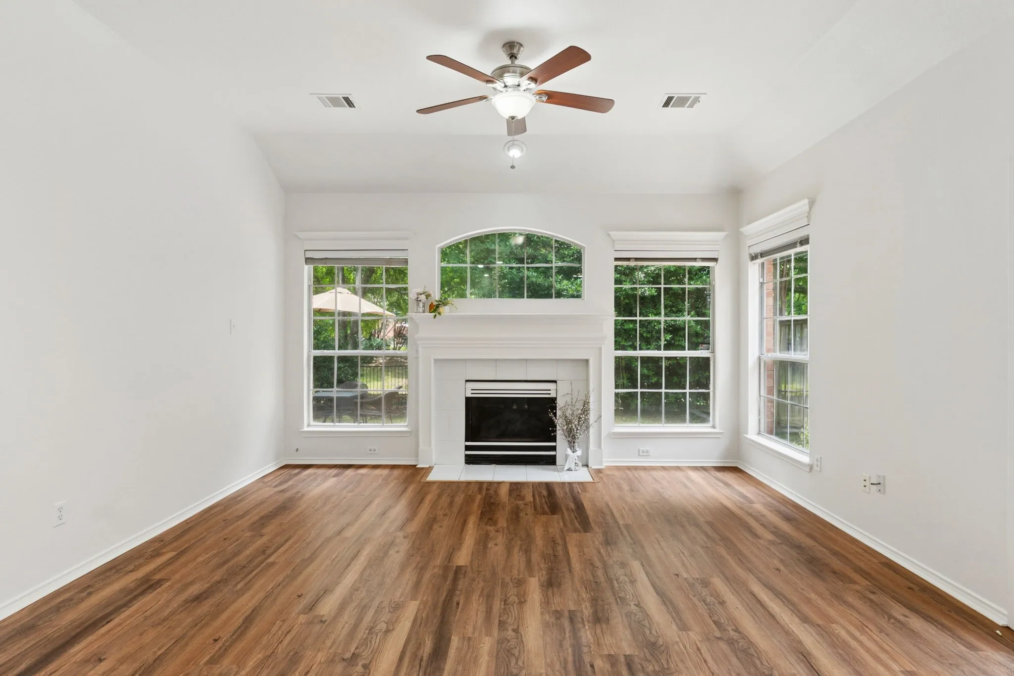 Wood-finish flooring, white fireplace with hearth, arched window, and ceiling fan